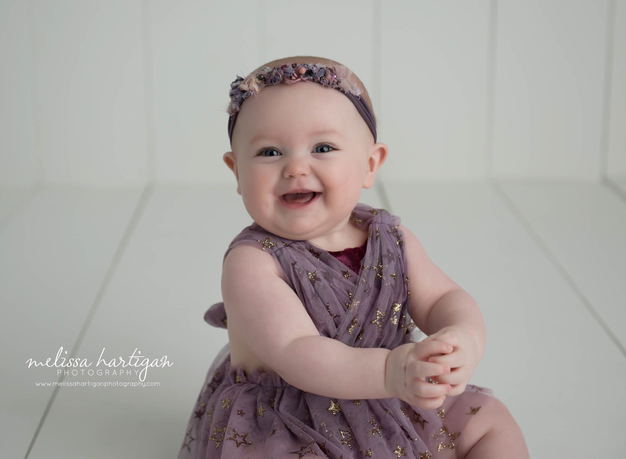 baby girl sitting smiling at camera wearing purple outfit with gold stars Baby photographer Connecticut