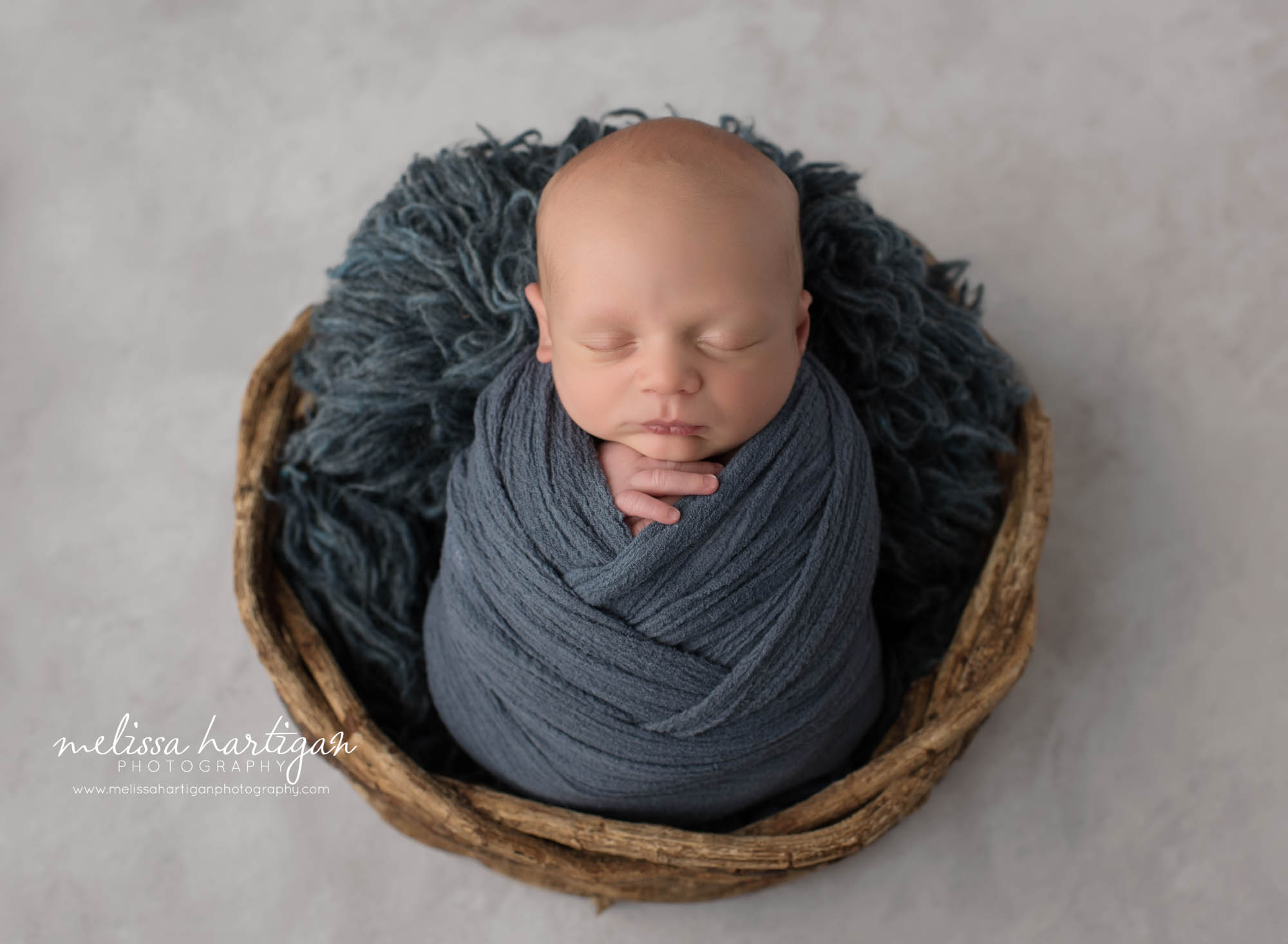 newborn baby boy wrapped in navy blue wrap with navy blue flokati piece in wicker basket CT newborn photographers