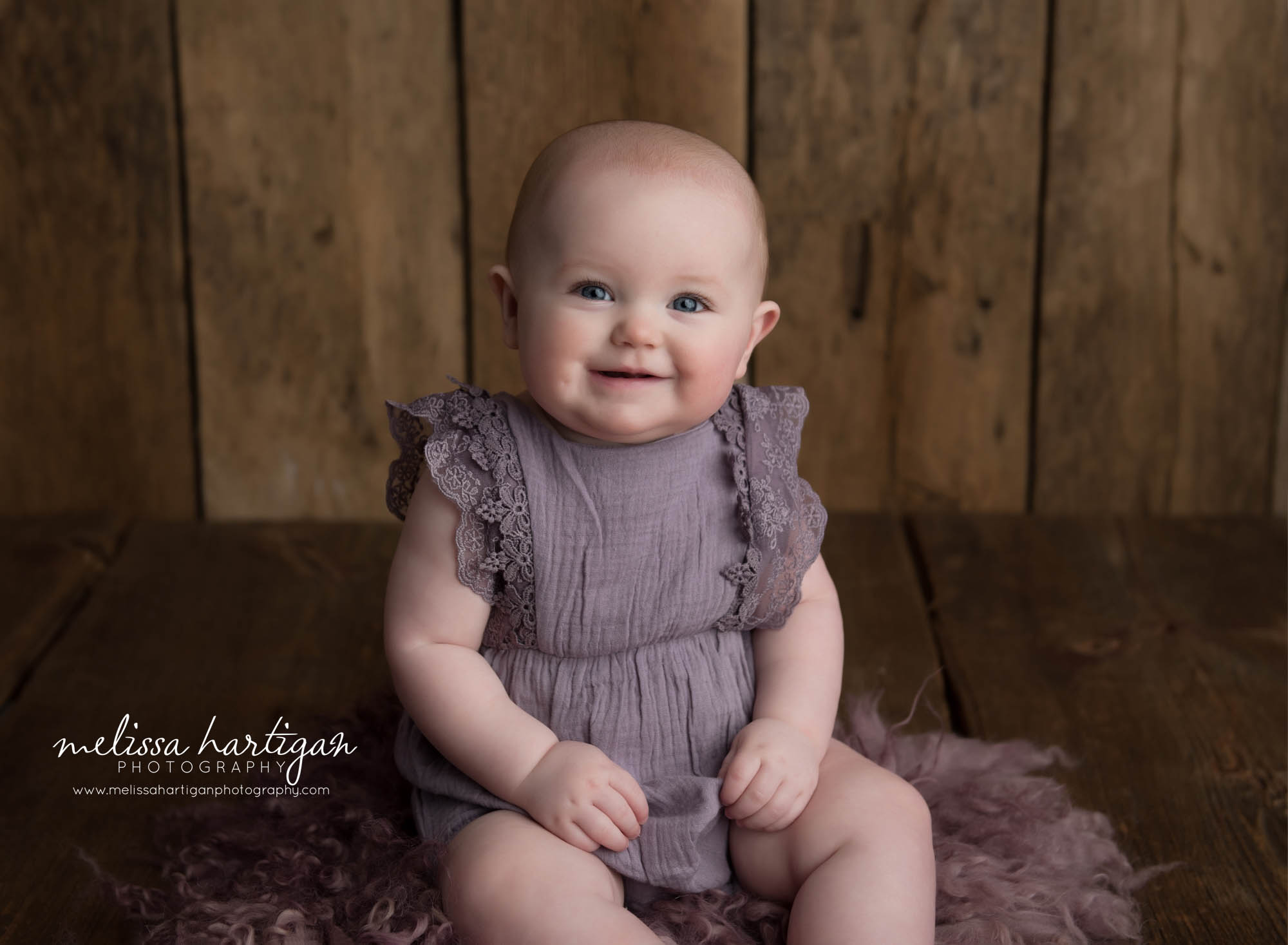 baby girl sitting on purple fluff layer looking at camera smiling