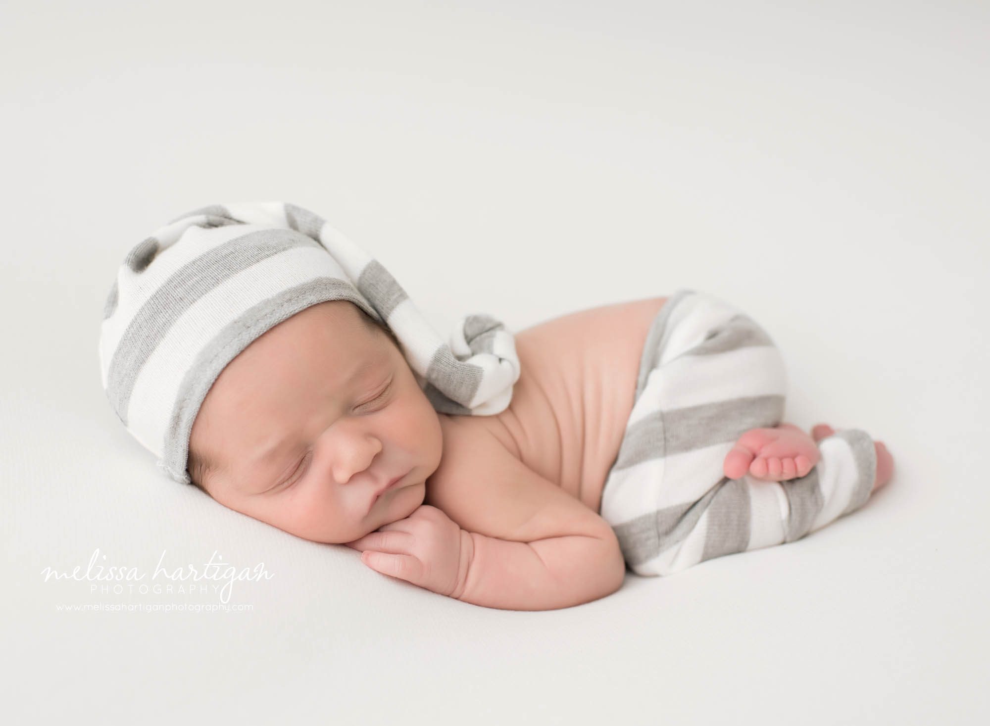 Newborn baby boy posed on tummy wearing white and gray striped sleepy cap and pants Connecticut Newborn Photography