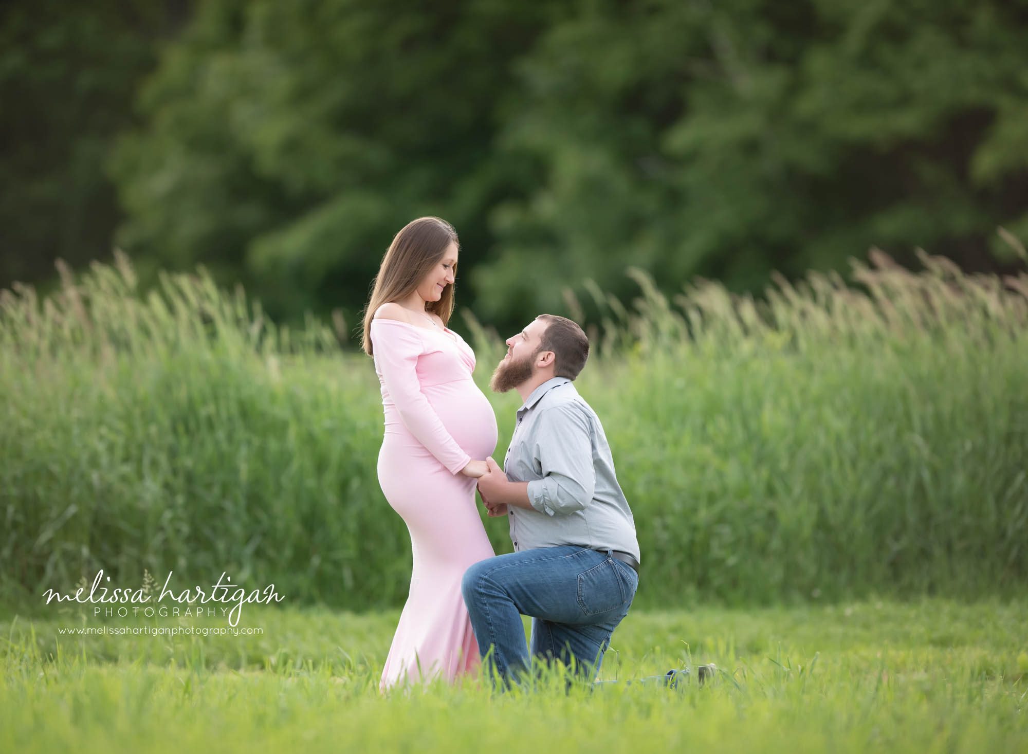 dad to be kneeling down holding pregnant wife's hands looking at eachother