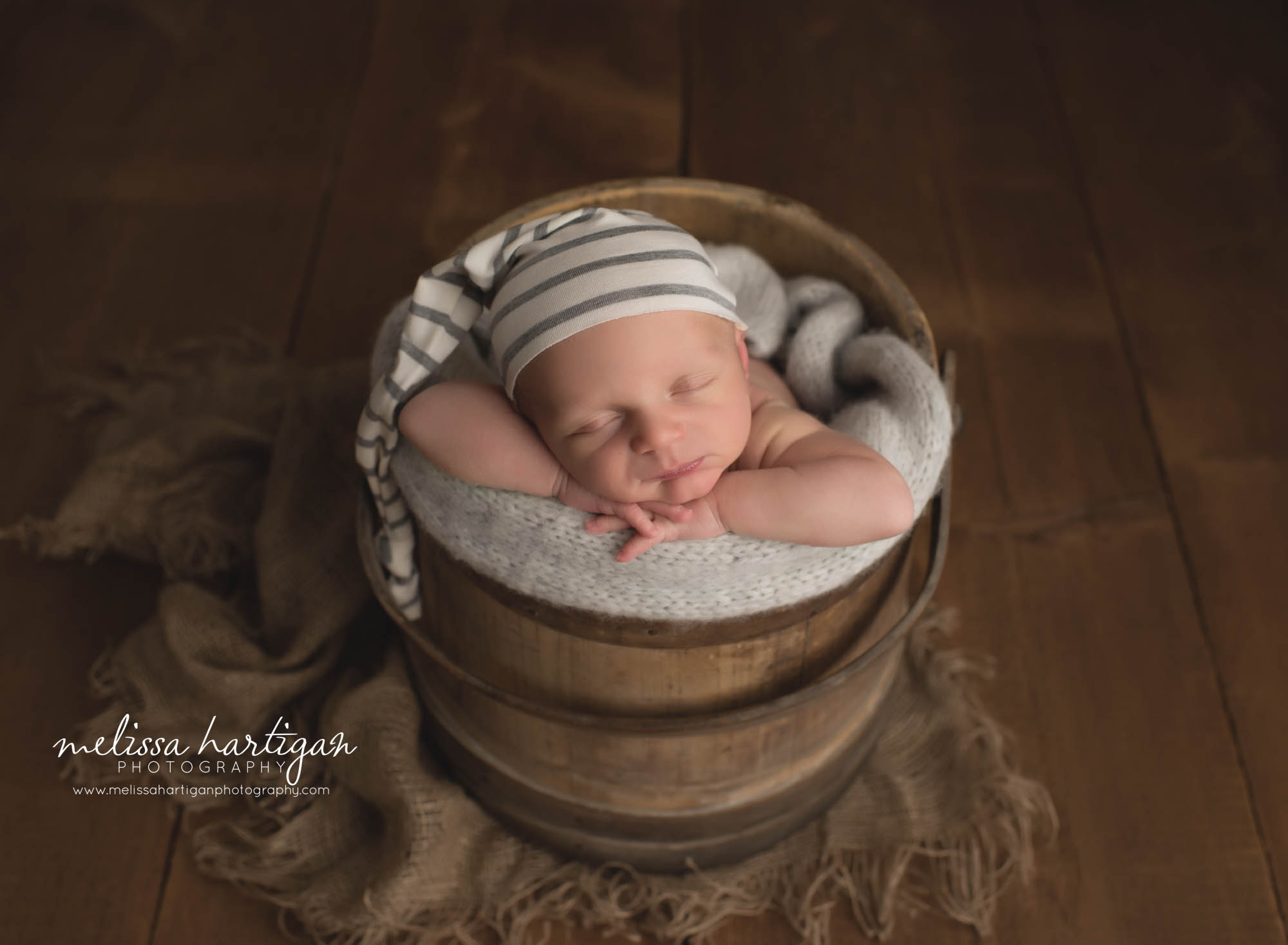Sleeping baby boy posed in wooden barrel with white and gray stripped sleepy cap