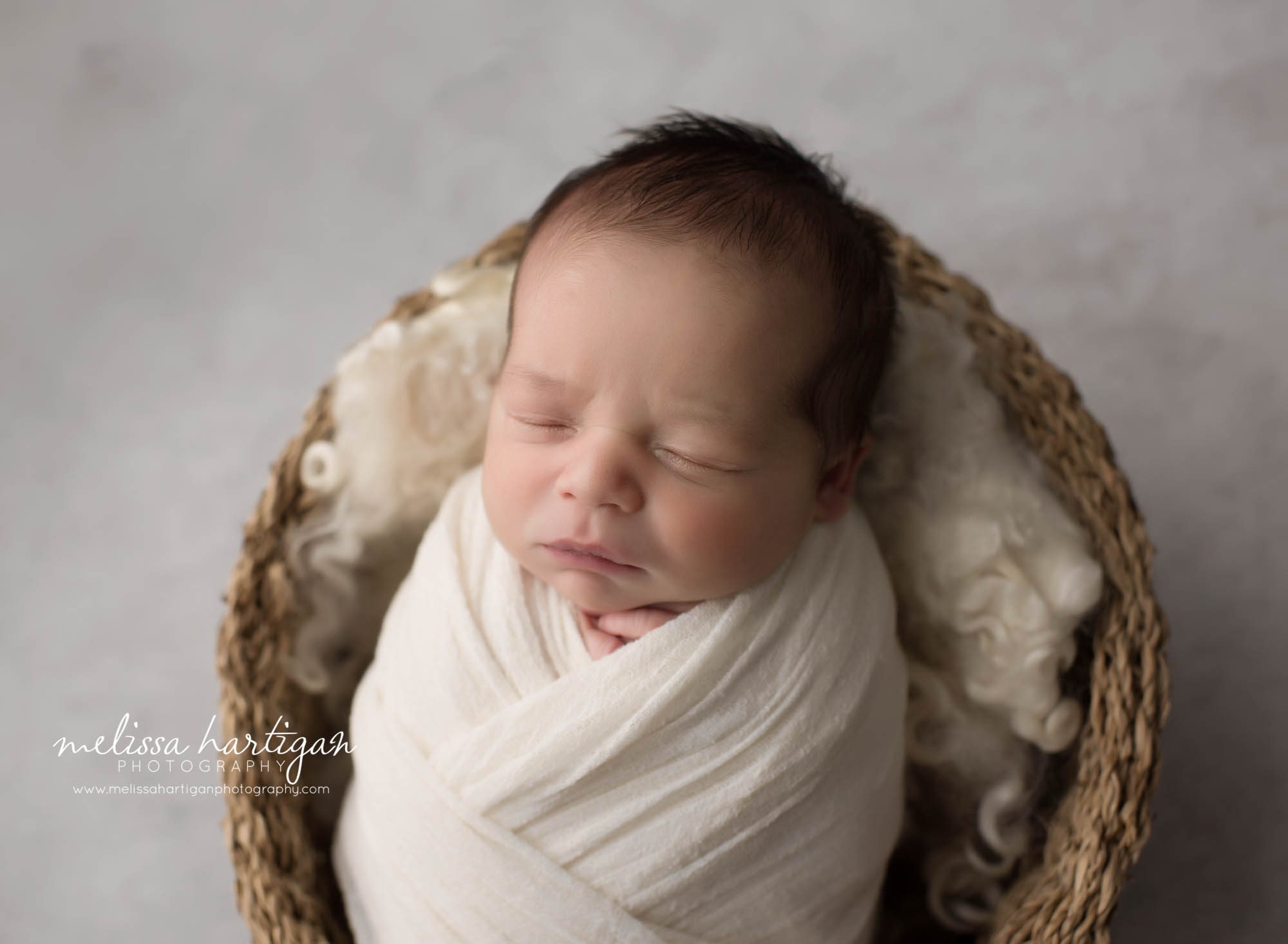 Baby boy wrapped in cream wrpa posed in wicker basket