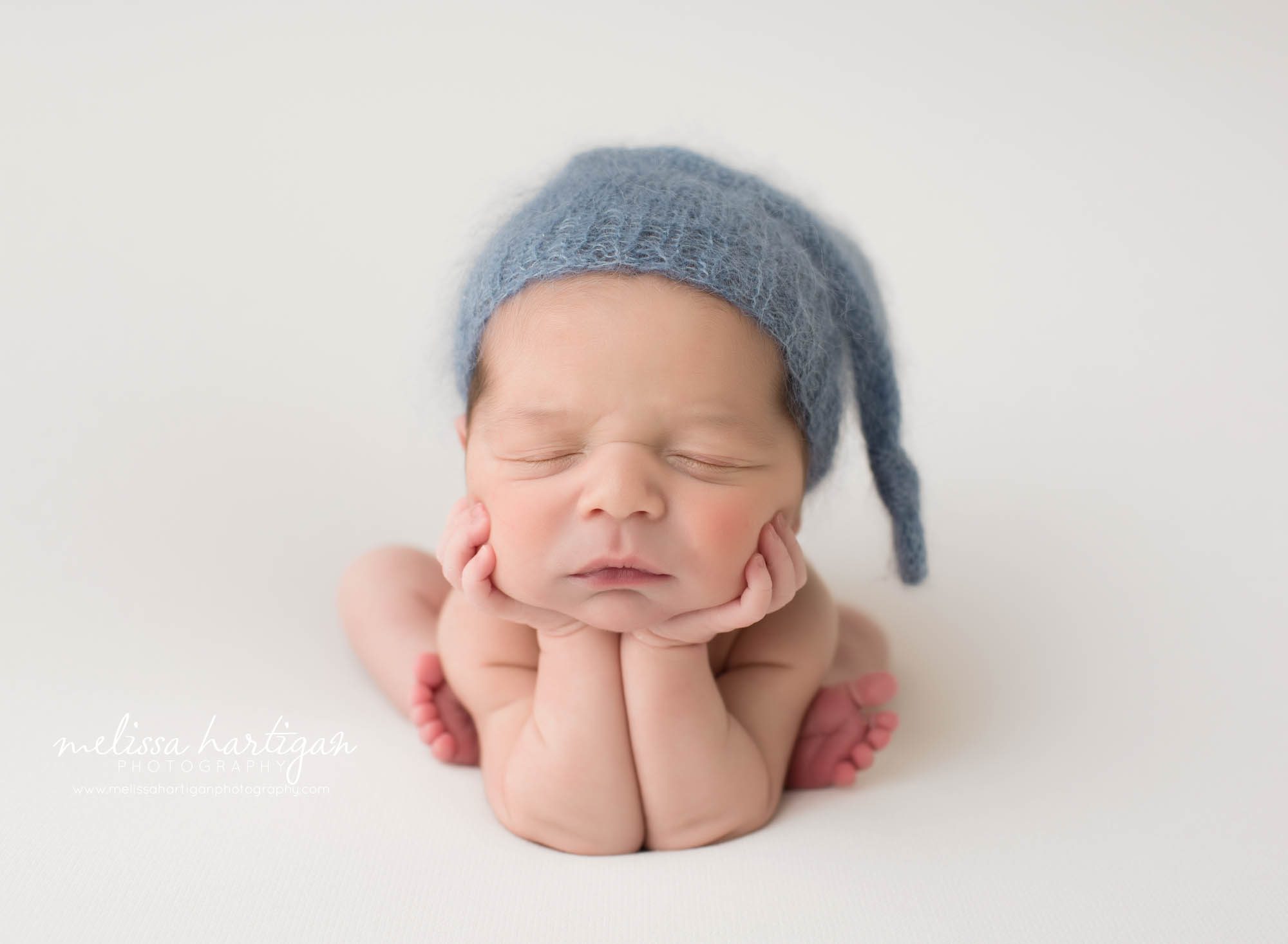 Newborn baby boy posed in froggy pose with blue knitted sleepy cap