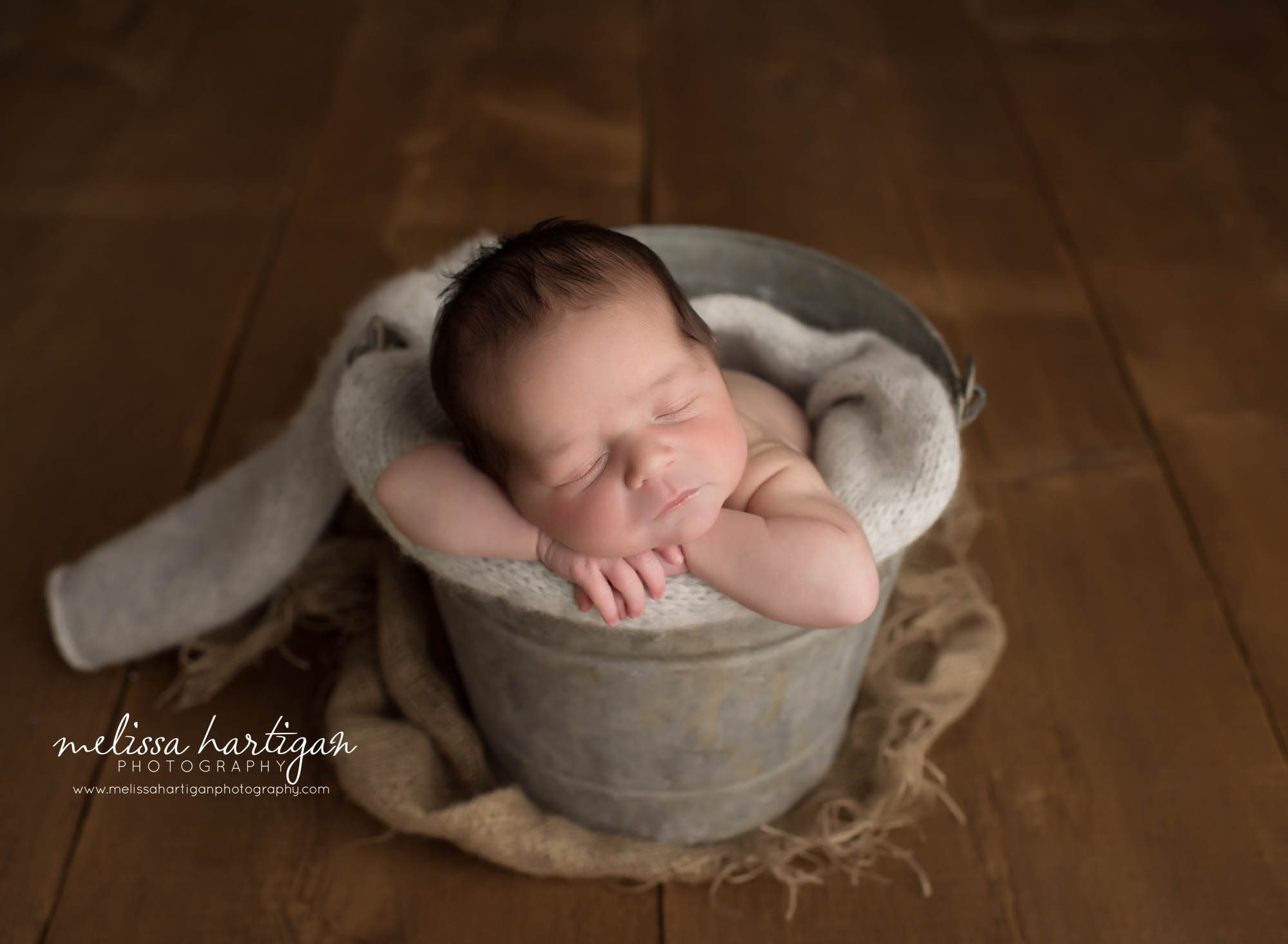Baby boy posed in metal bucket with light gray knitted wrap around bucket
