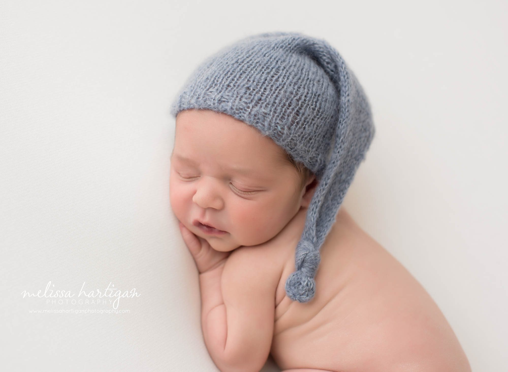 Newborn baby boy posed on side with knitted blue sleepy cap