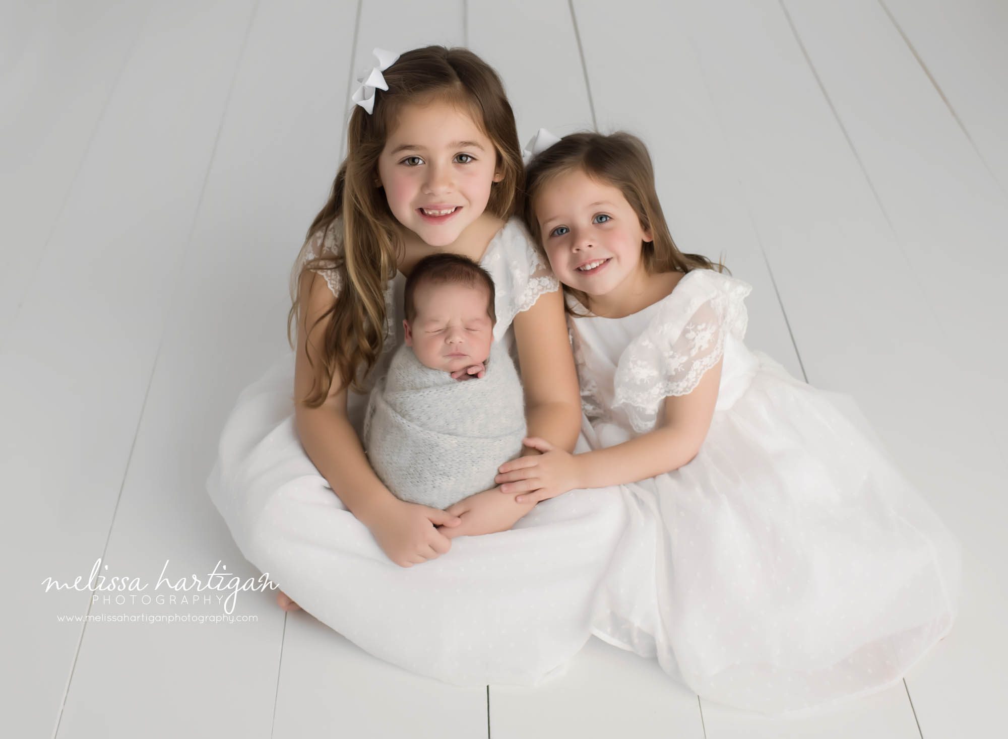 Two big sisters posing with new baby brother wrapped in knitted wrap sibling photo in newborn session captured in Connecticut newborn photography studio