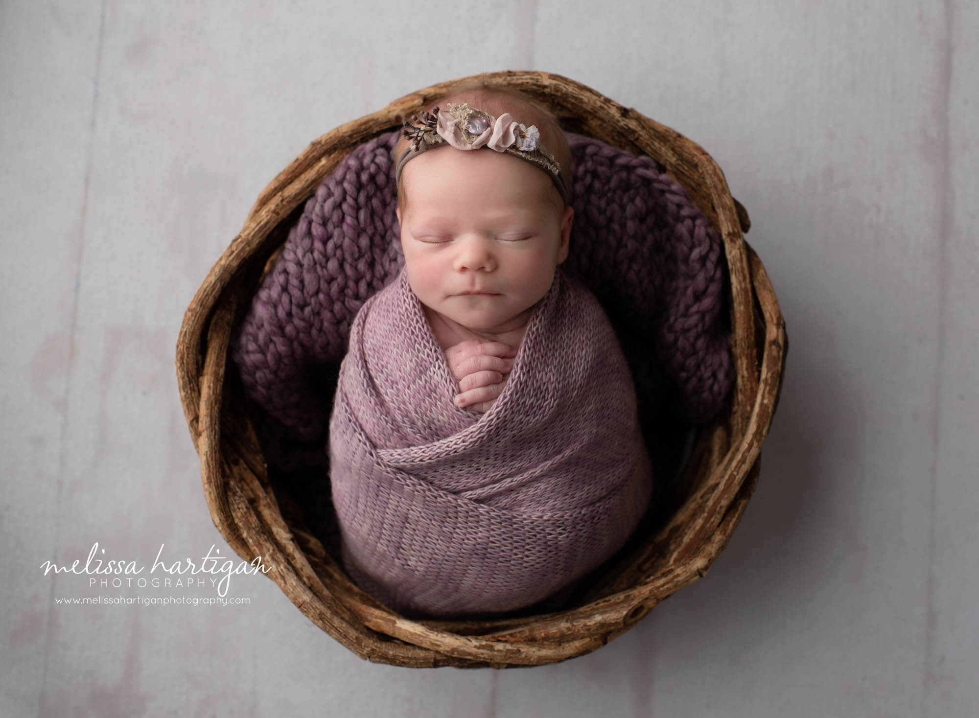 newbonr baby girl wrapped in purple wrap with flower headband purple layer and wicker basket
