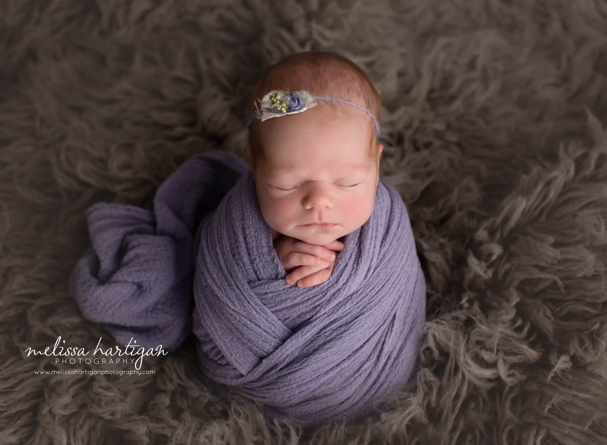 newborn baby girl wrapped in purple wrap posed on grey gray flokati