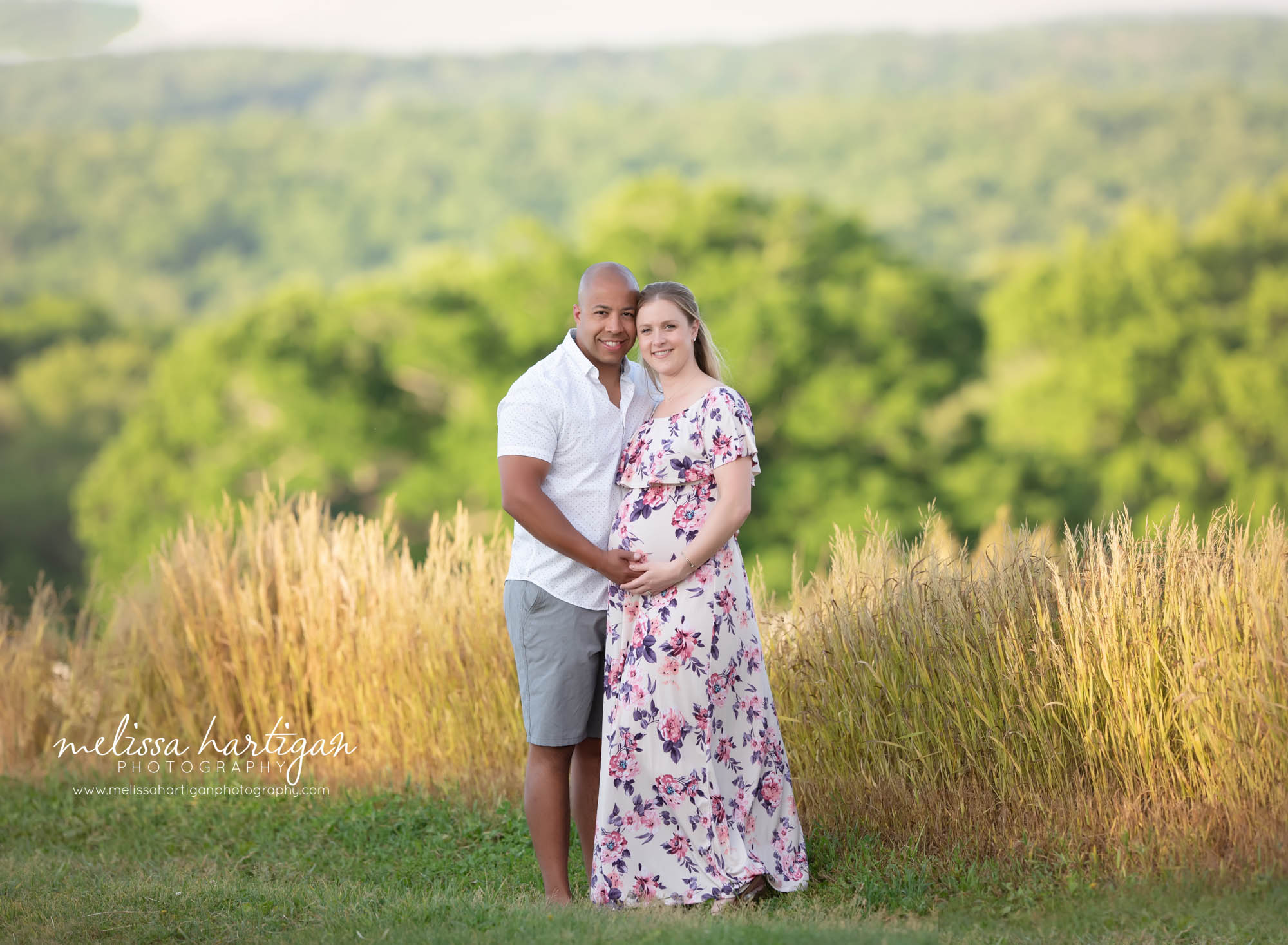 pregnancy mom wearing pink and purple floral dress standing couples maternity picture with mom-to-be and dad-to-be