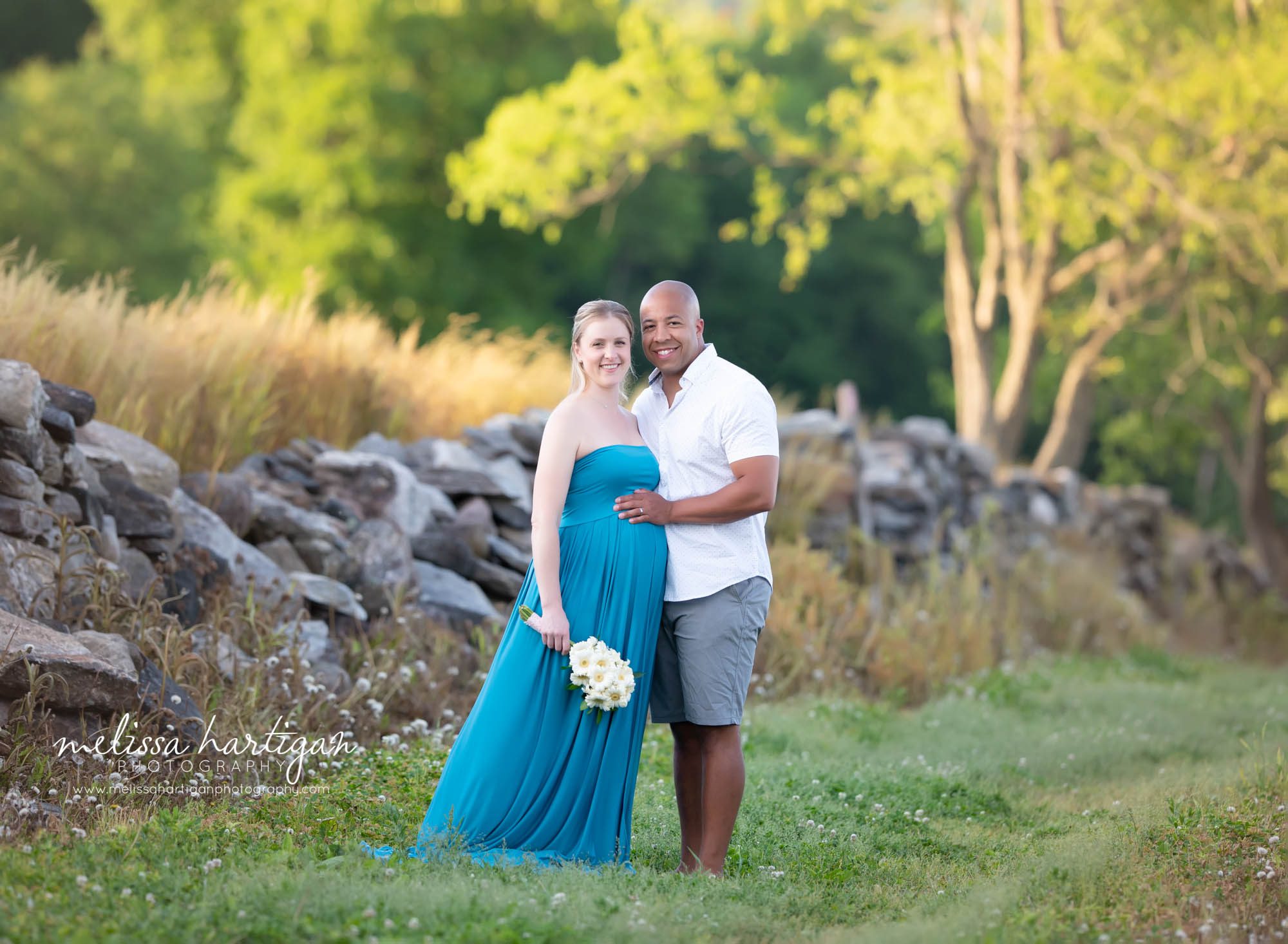 pregnant momwearing bright turquoise maternity dress dad holding moms baby bump mom holding bouquet of flowers Manchester Maternity Photographer