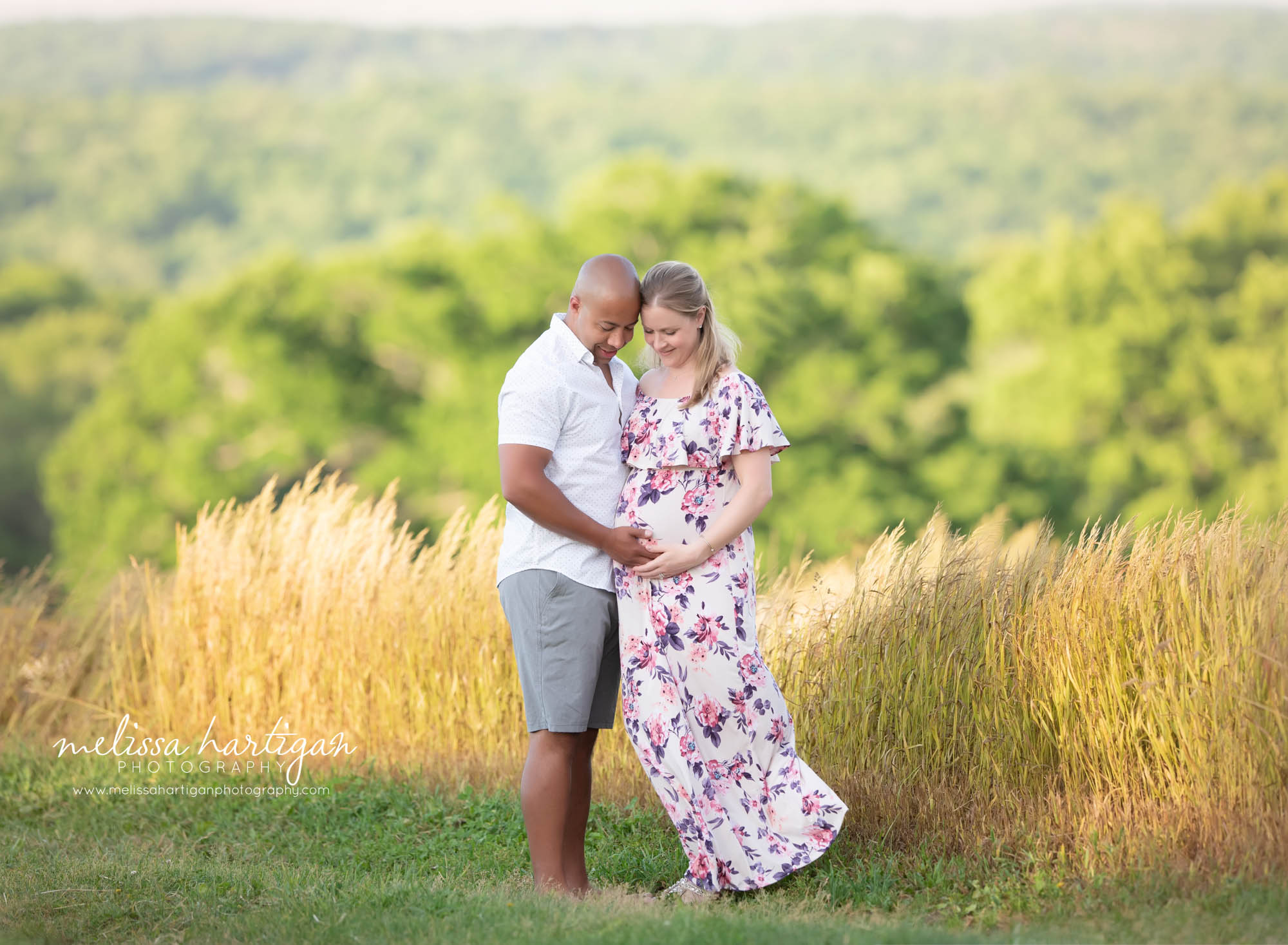 expectant couple touching foreheads looking down at moms baby bump holding hands and holding pregnant baby belly Maternity Photography Manchester CT