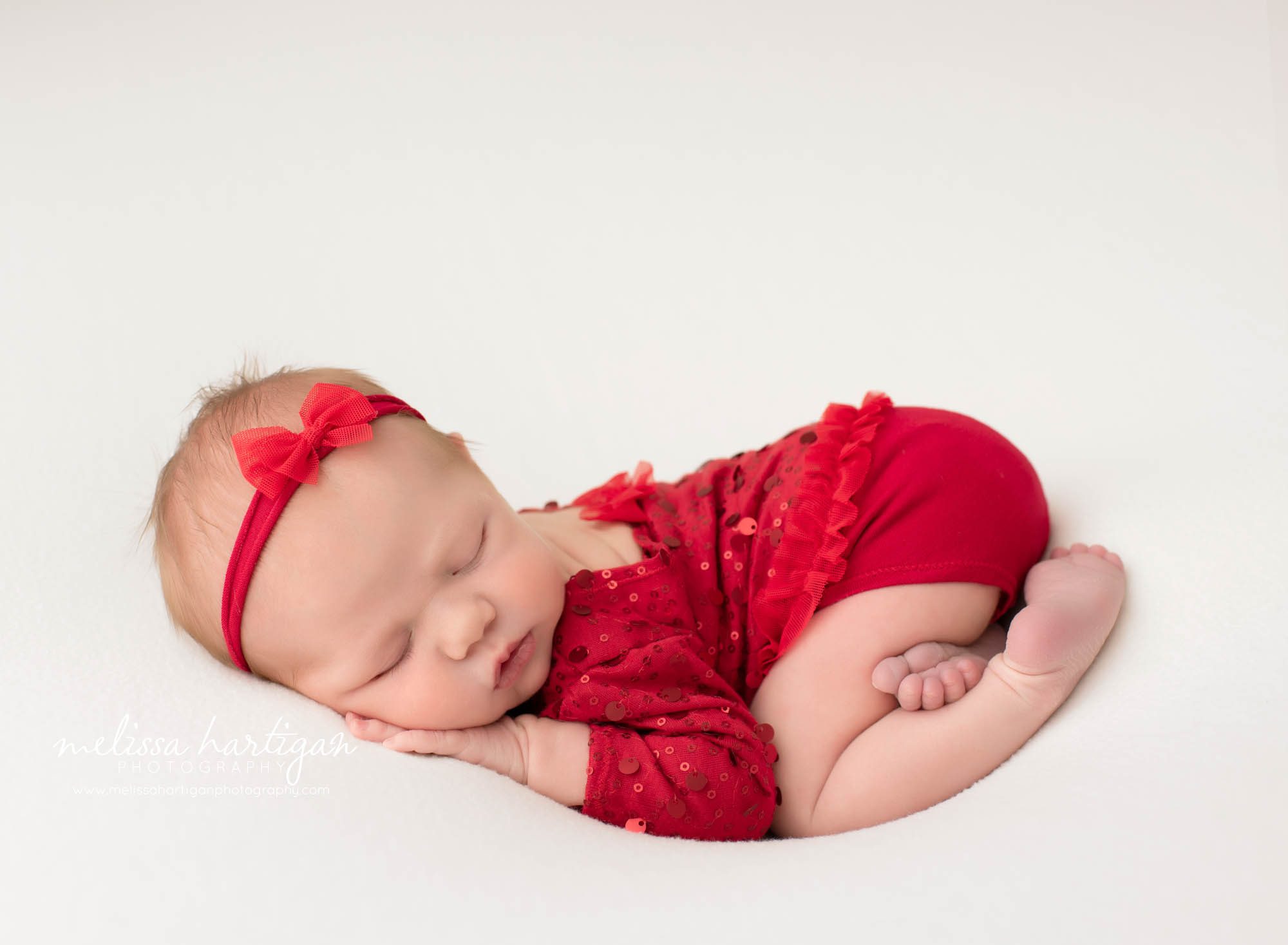 Newborn baby girl posed on tummy with red bow headband and red sequined outfit Mansfield CT newborn Baby Photography