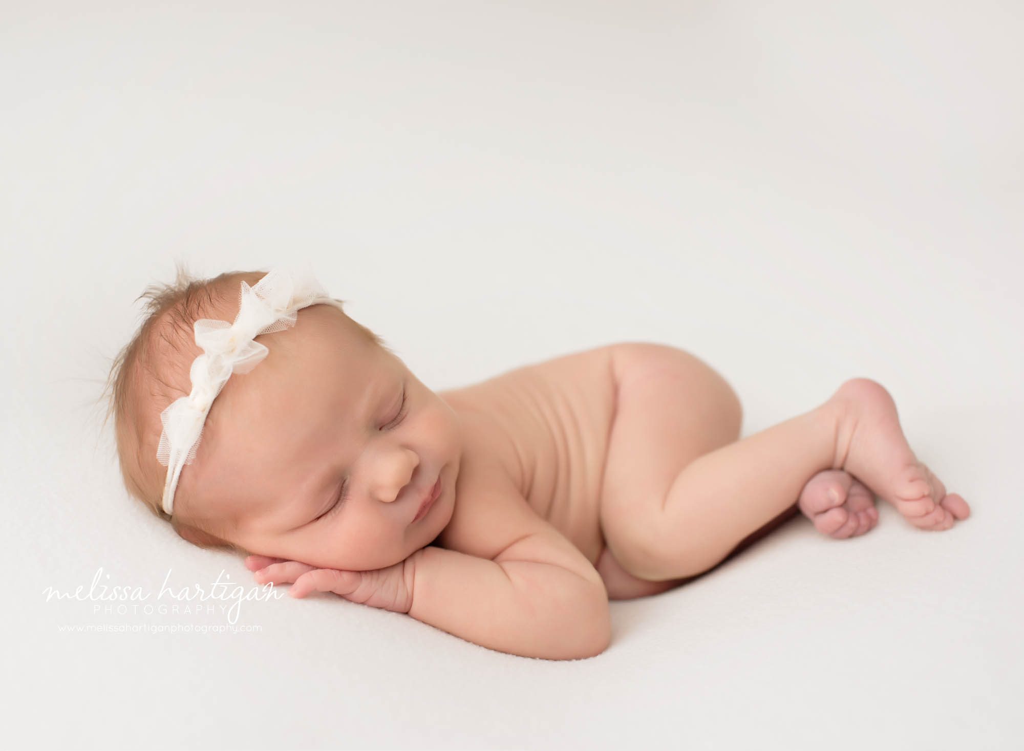 Newborn baby girl posed on side with bow headband