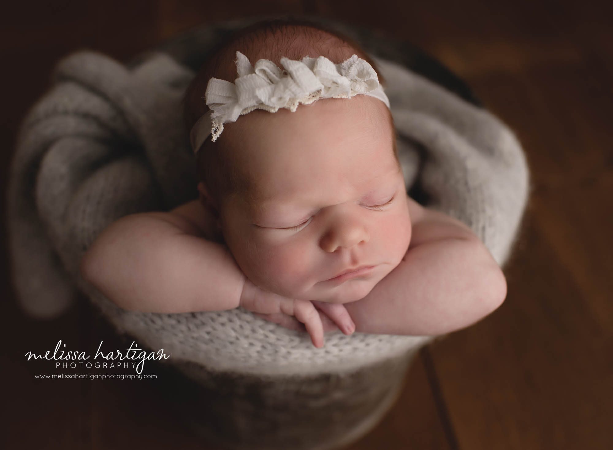 Newborn baby girl posed in bucket with chin on hands bow headband