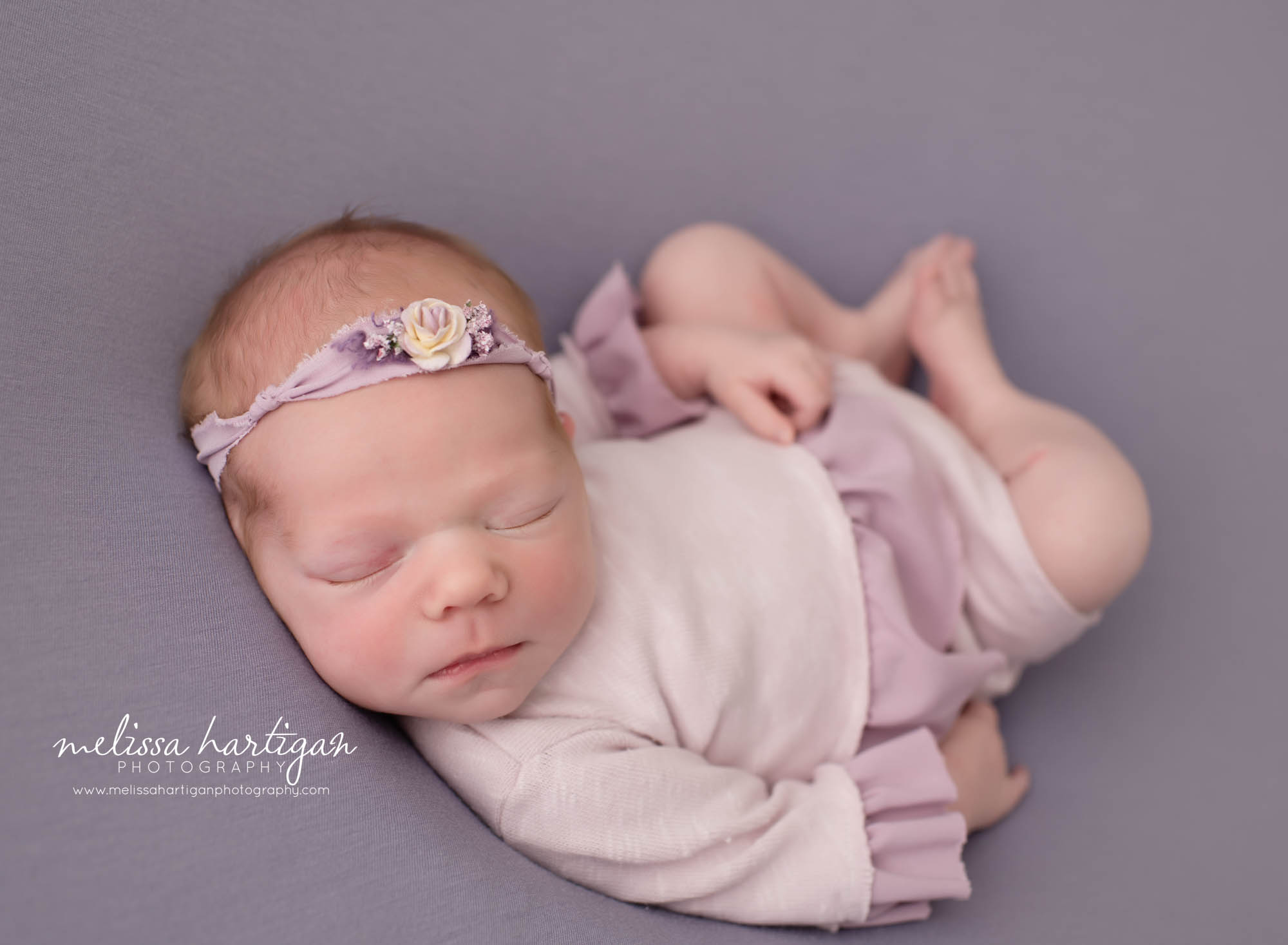newborn baby girl pose don back in huck finn newborn photography pose wearing light purple outfit and flower headband Newborn Photography Vernon CT