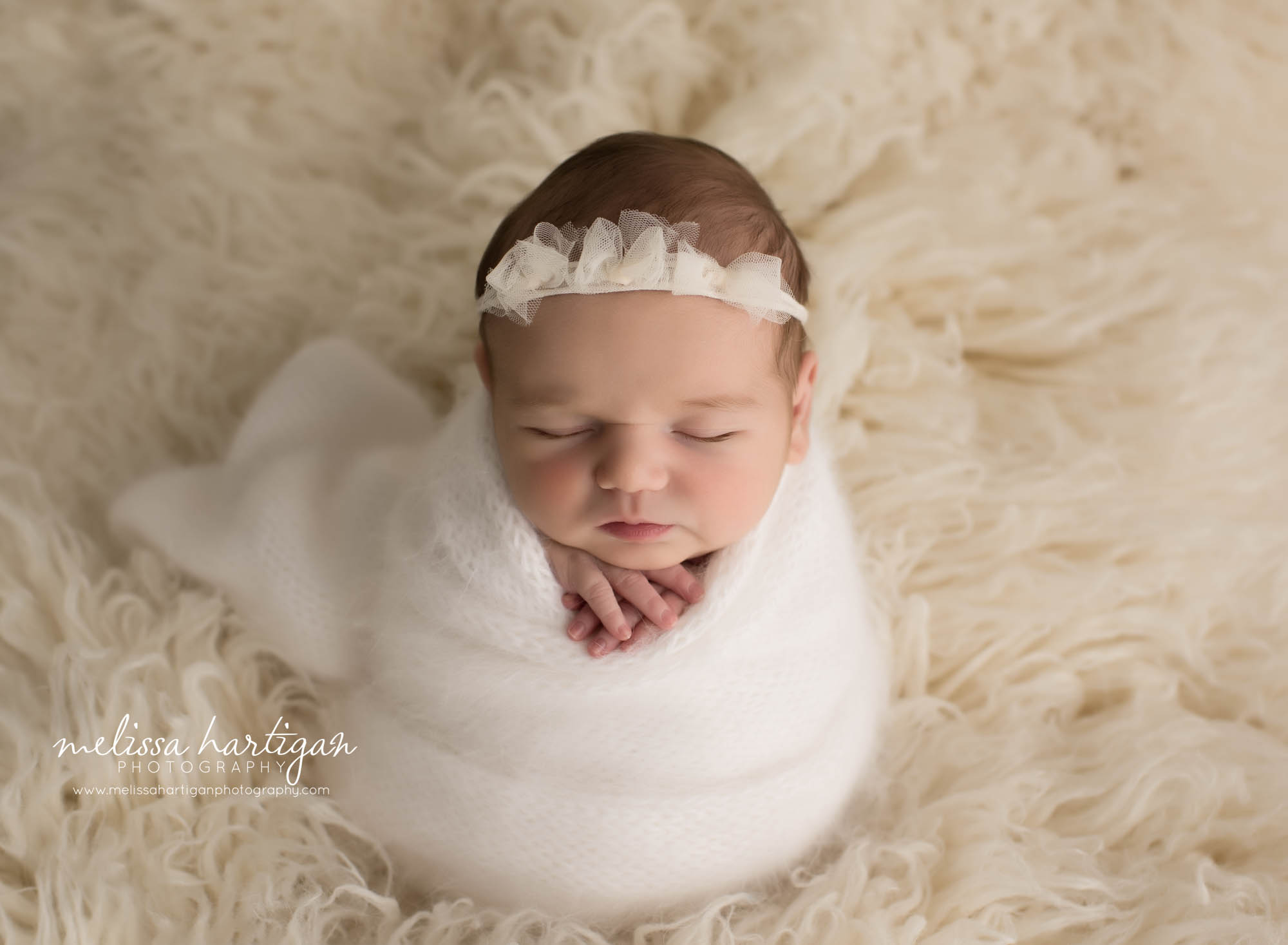 newborn baby girl wrapped in white and cream knitted wrap with bow headband
