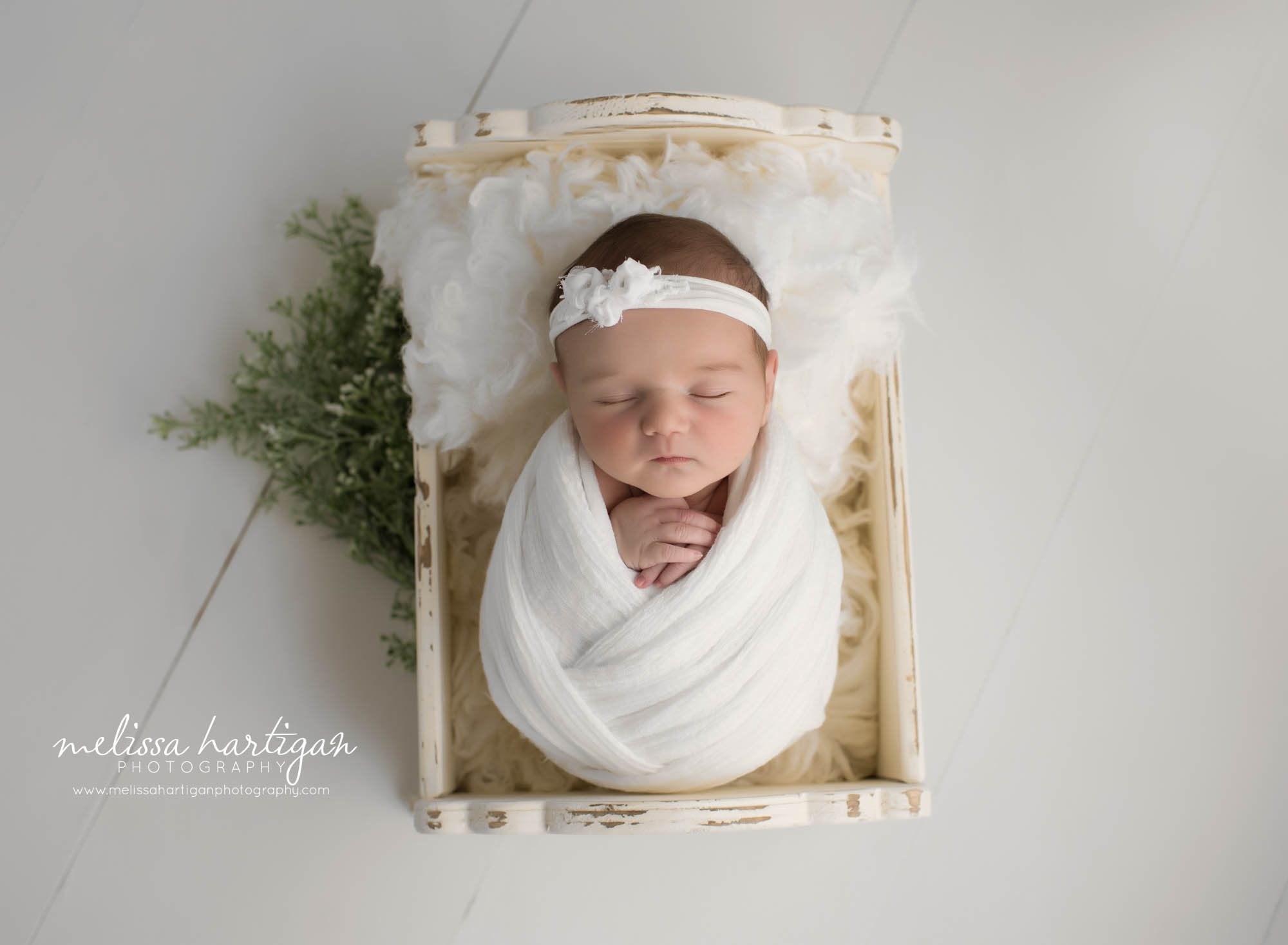 newborn baby girl posed in wooden cradle wrapped in white wrap with white headband