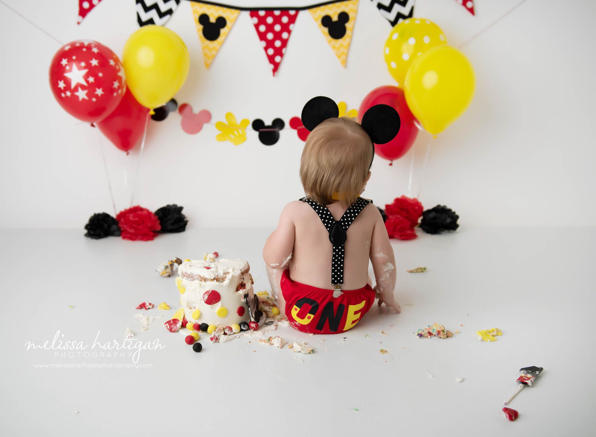 baby boy sitting with back to camera iwth mickey mouse cake smash