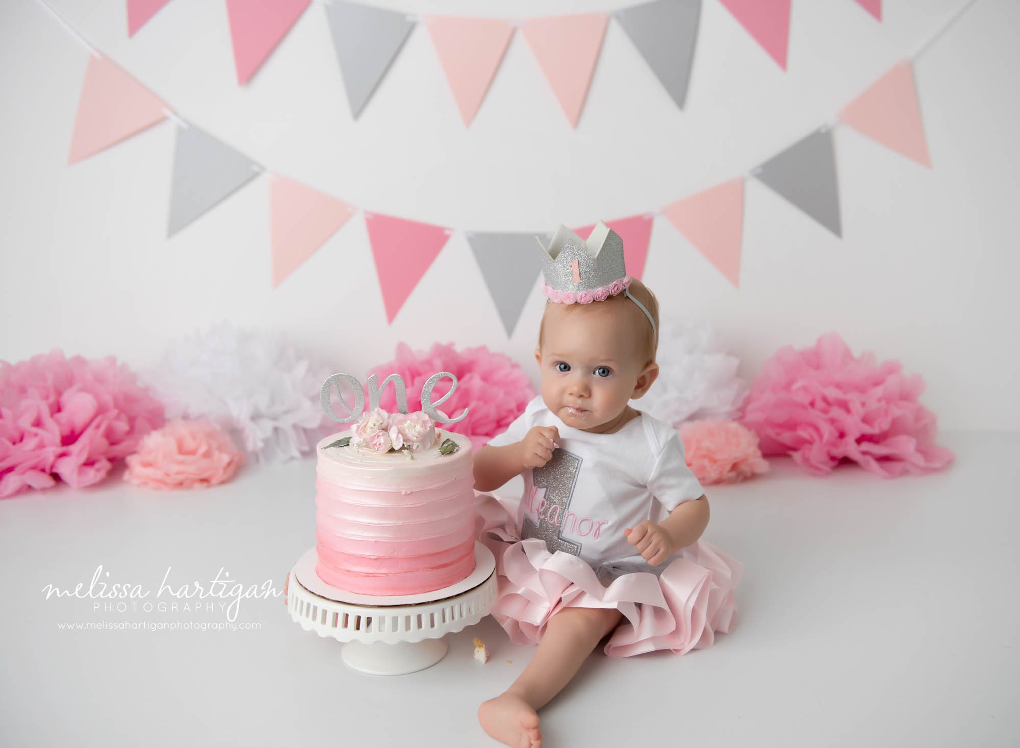 baby girl sitting on floor in studio eating cake from cake smash pictures