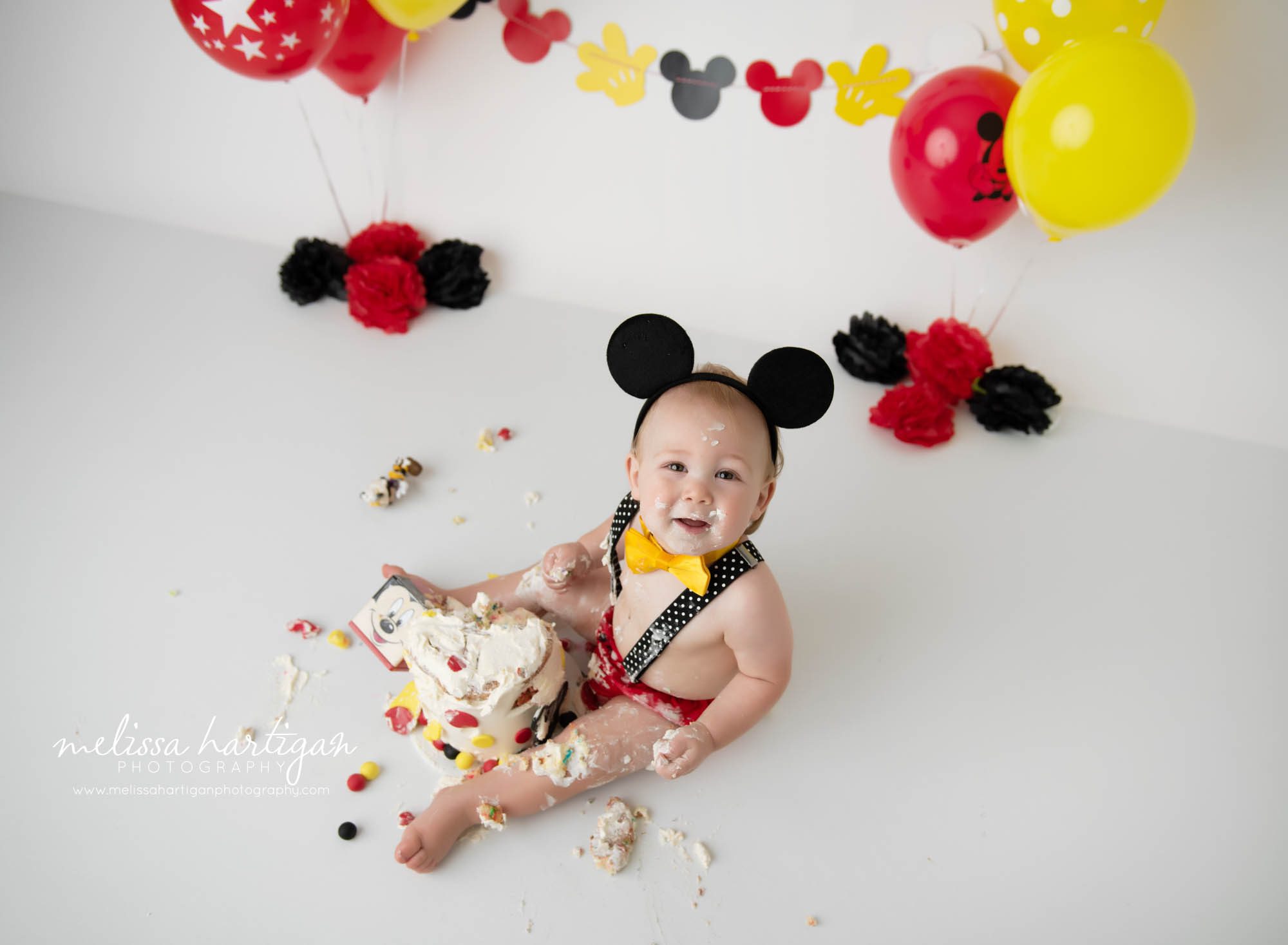 baby boy sitting on floor with destroyed mickey mouse cake smash