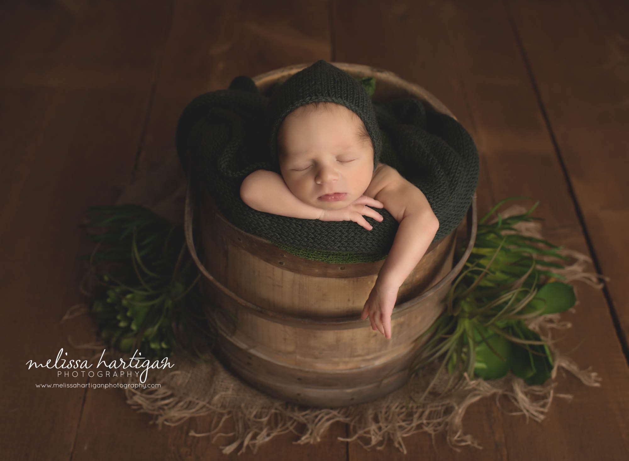 newborn baby boy posed in wooden bucket with dark green bonnet wrap and foiliage Norwich CT baby Photography