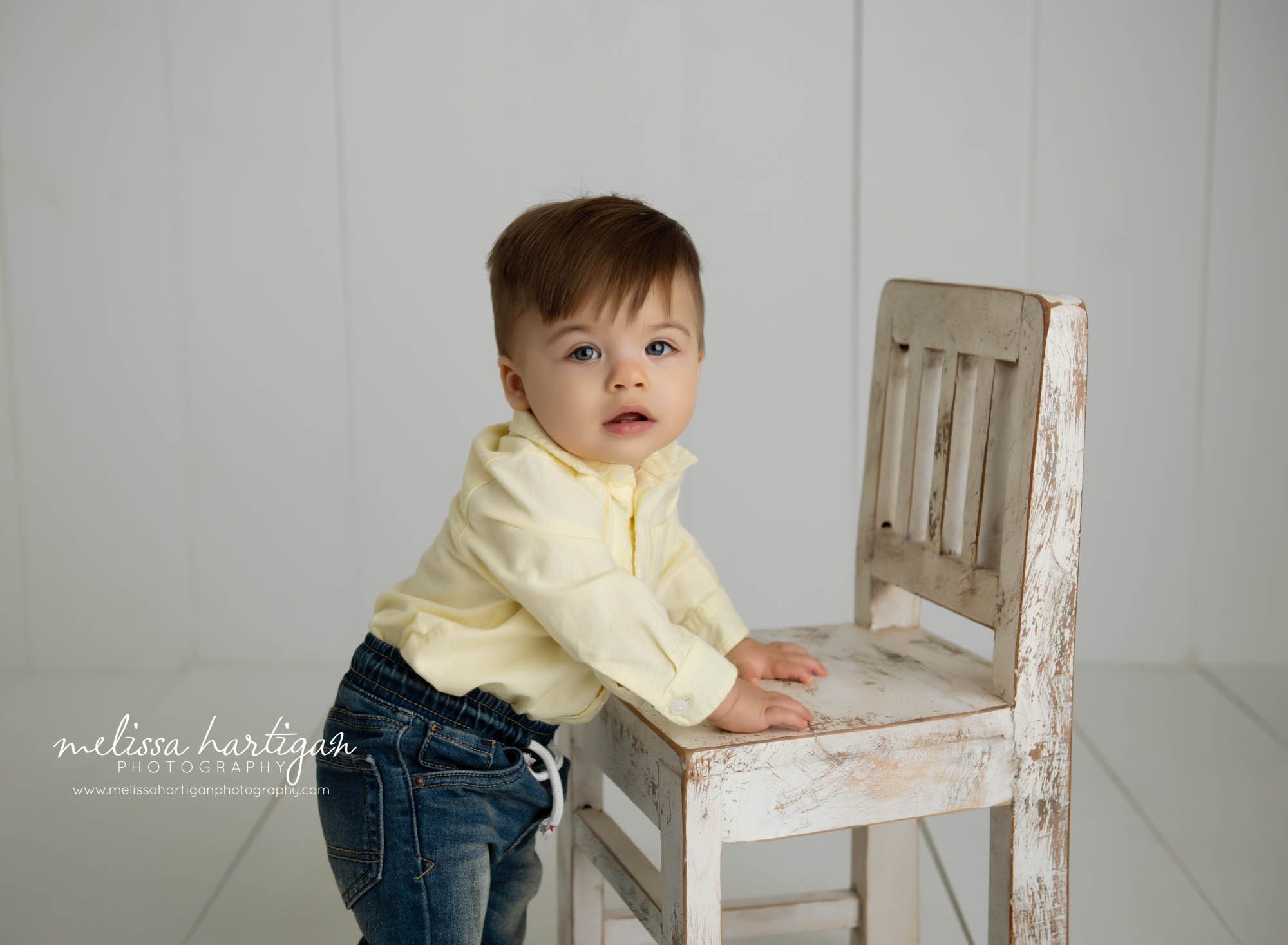 baby boy standing up at wooden chair milestone session