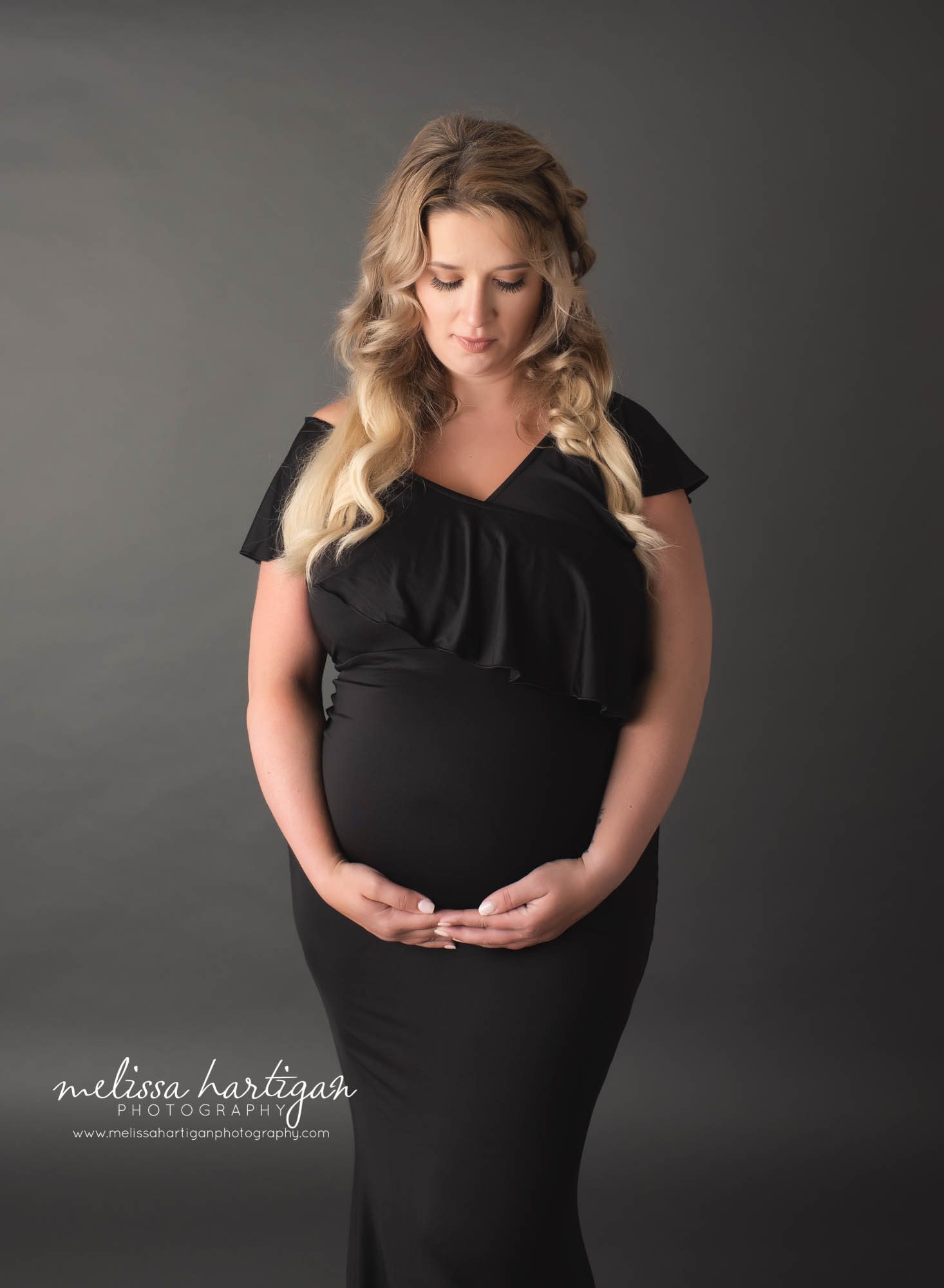 pregnant mom to be holding belly looking down wearing black maternity dress with ruffles around the bust