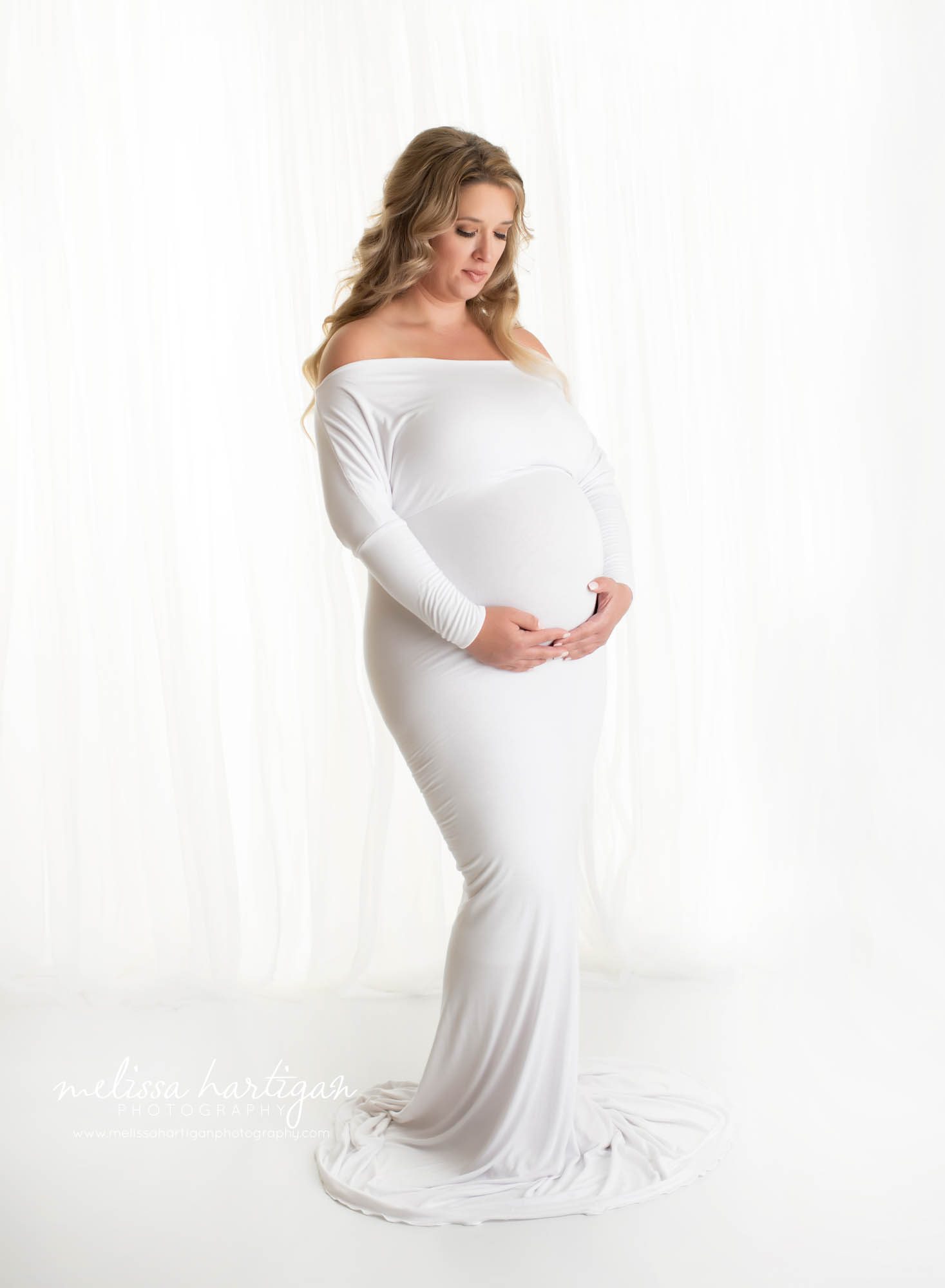 pregnant mom standing in photography studio holding belly wearing white maternity gown CT maternity Photography