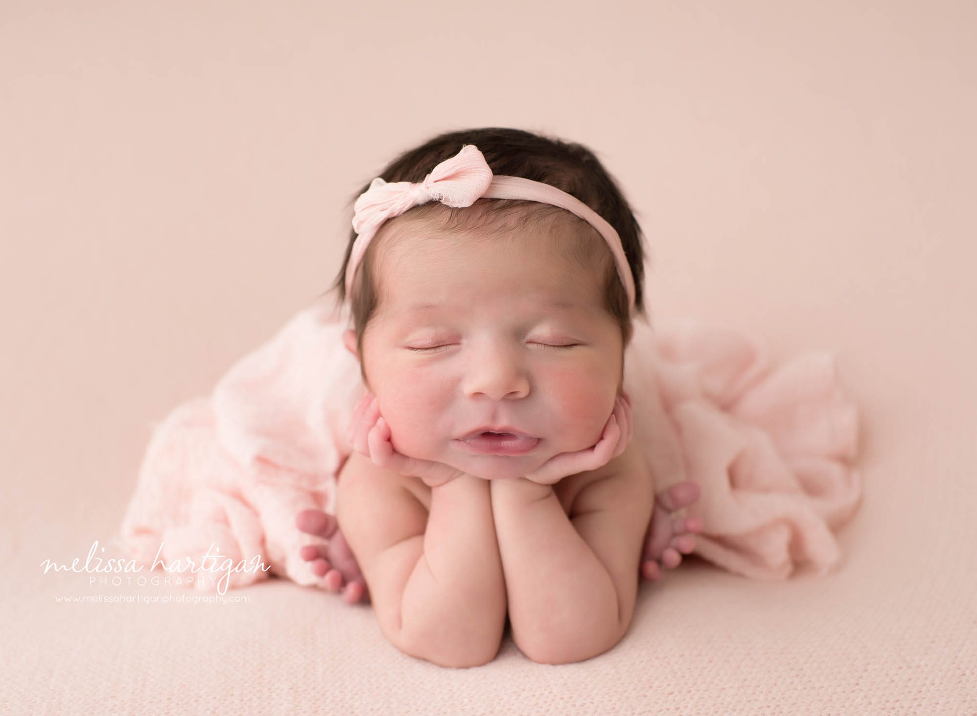 baby girl posed froggy pose on light pink backdrop with pink bow CT newborn photographer