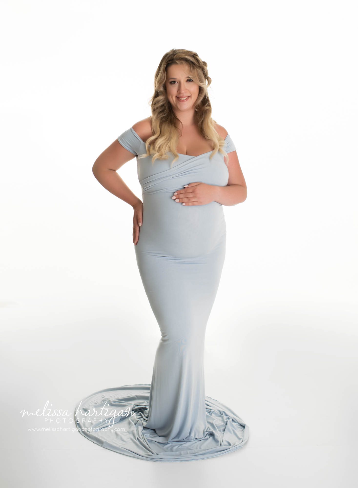 mom holding belly smiling wearing long form fitting light blue maternity gown enfield CT maternity Photography