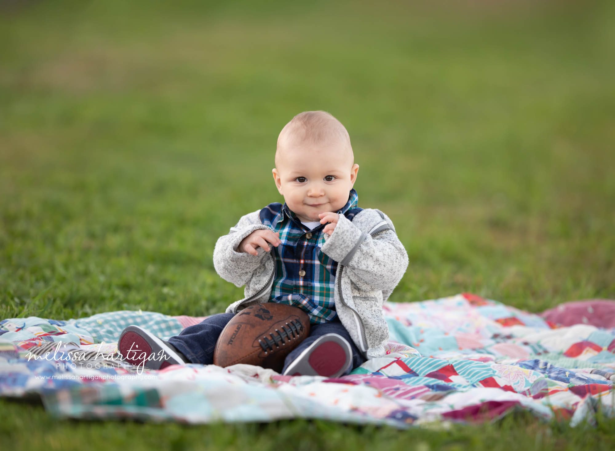 baby boy sitting on grass on blanket with football in his lap