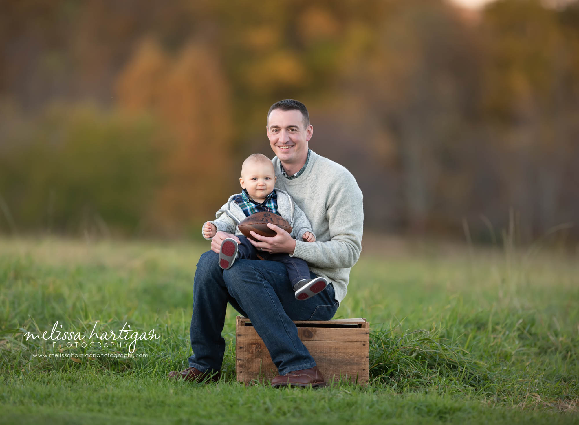 dad and baby son sitting on wooden crate holding a football