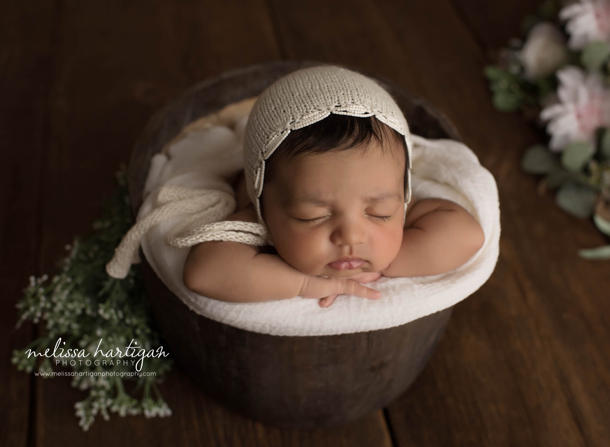 baby girl posed in brown wooden bucket with cream knitted bonnet and greenery elements