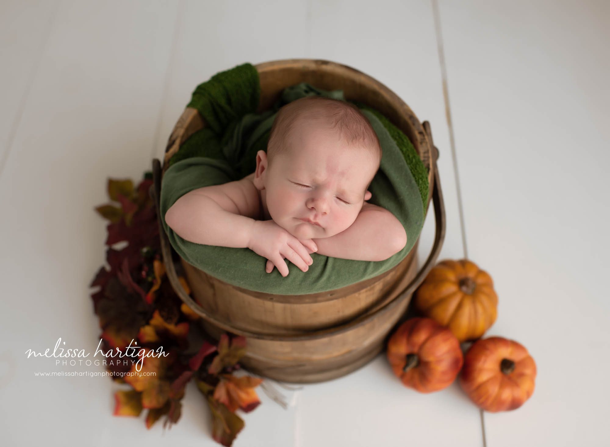 baby boy posed in wooden barrel with green burnt orange and red tinges in colors for foliage and pumpkin props Mansfield CT newborn Photography