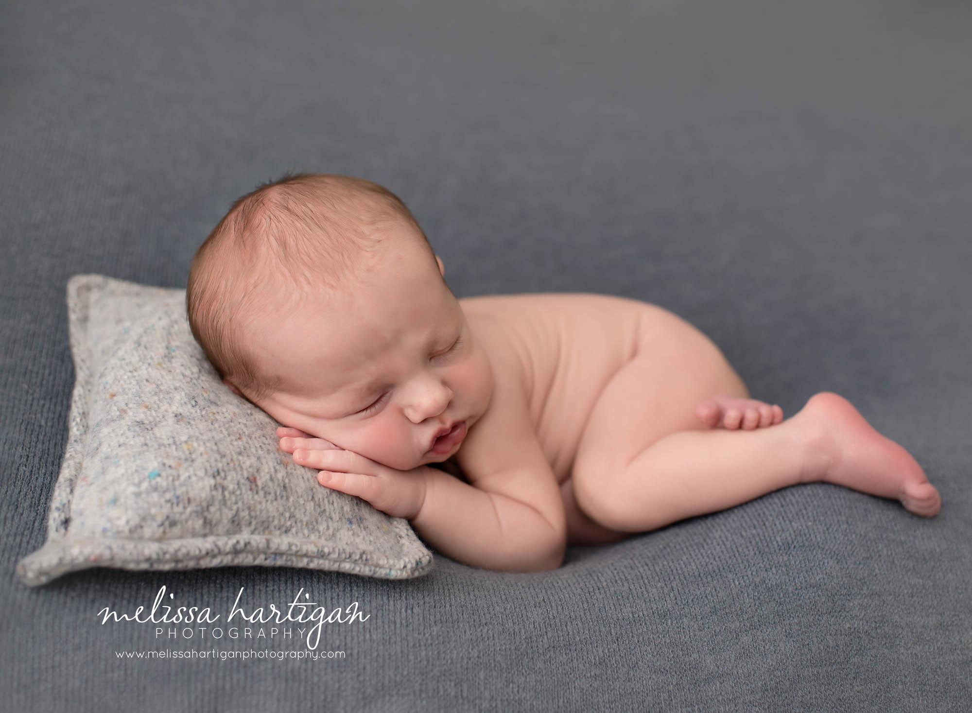 baby boy pose don blue backdrop with grey newborn pillow