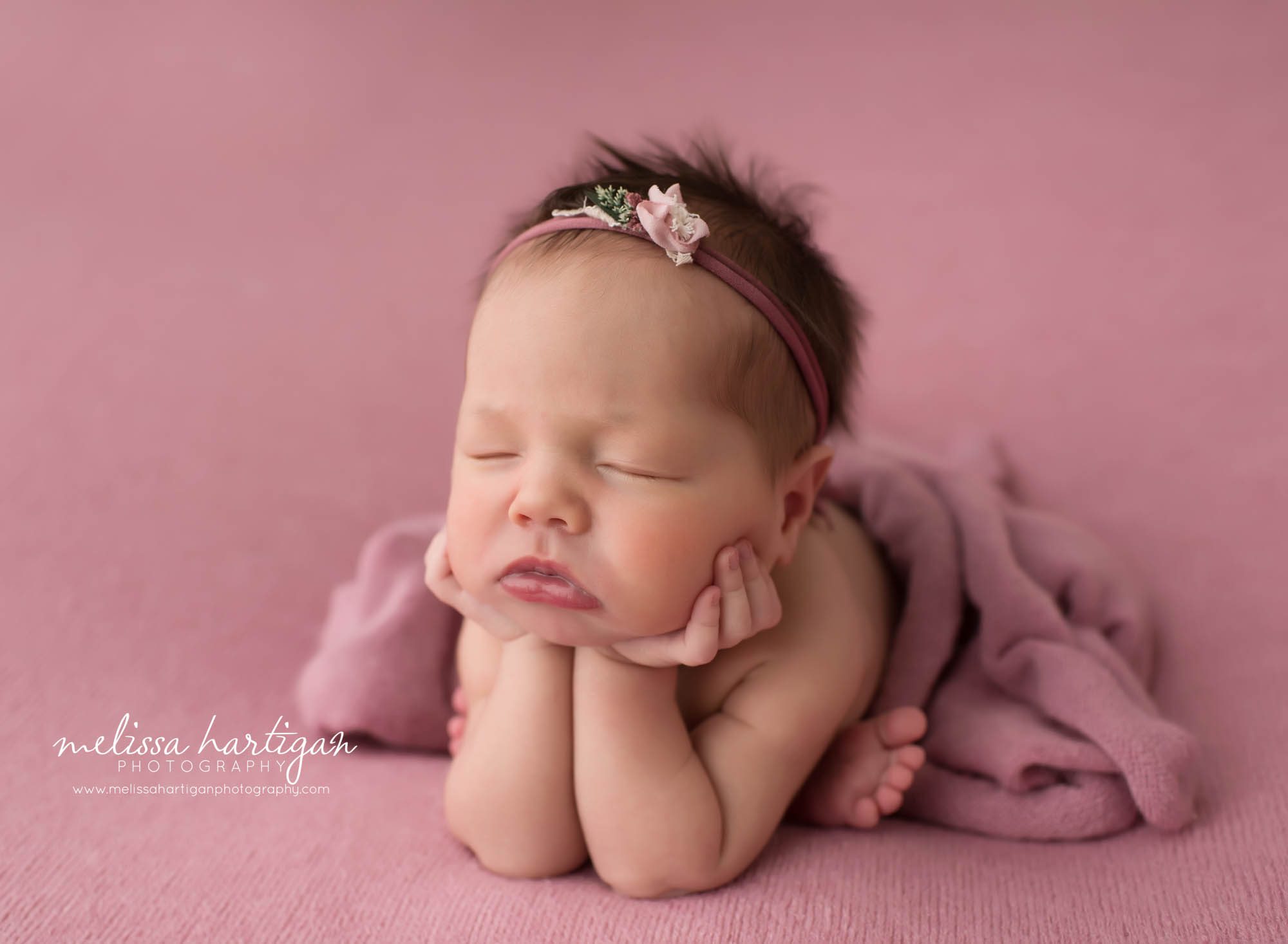 newborn baby girl posed froggy pose with pink wrap and backdrop