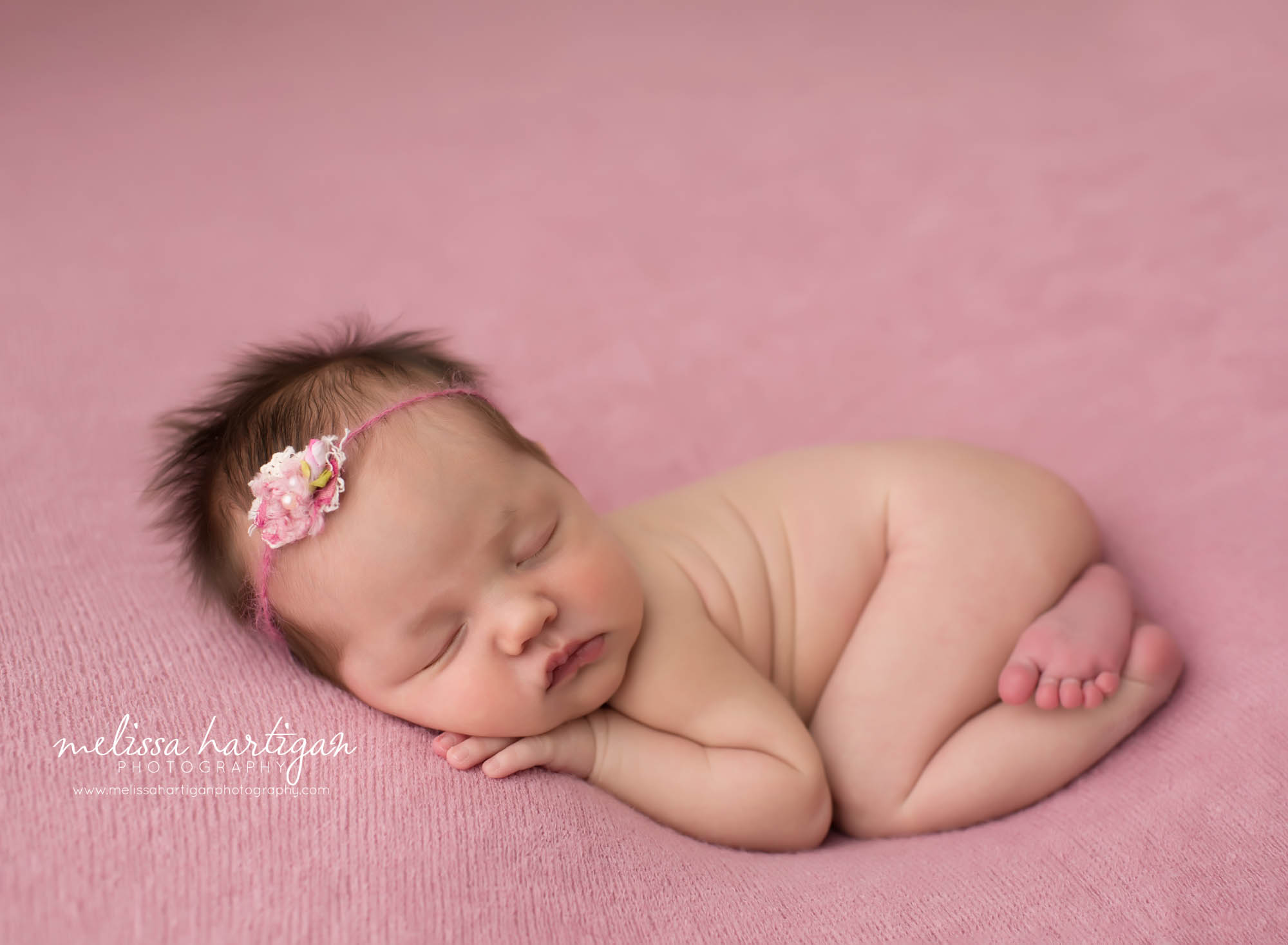 newborn baby girl posed on pink backdrop with headband