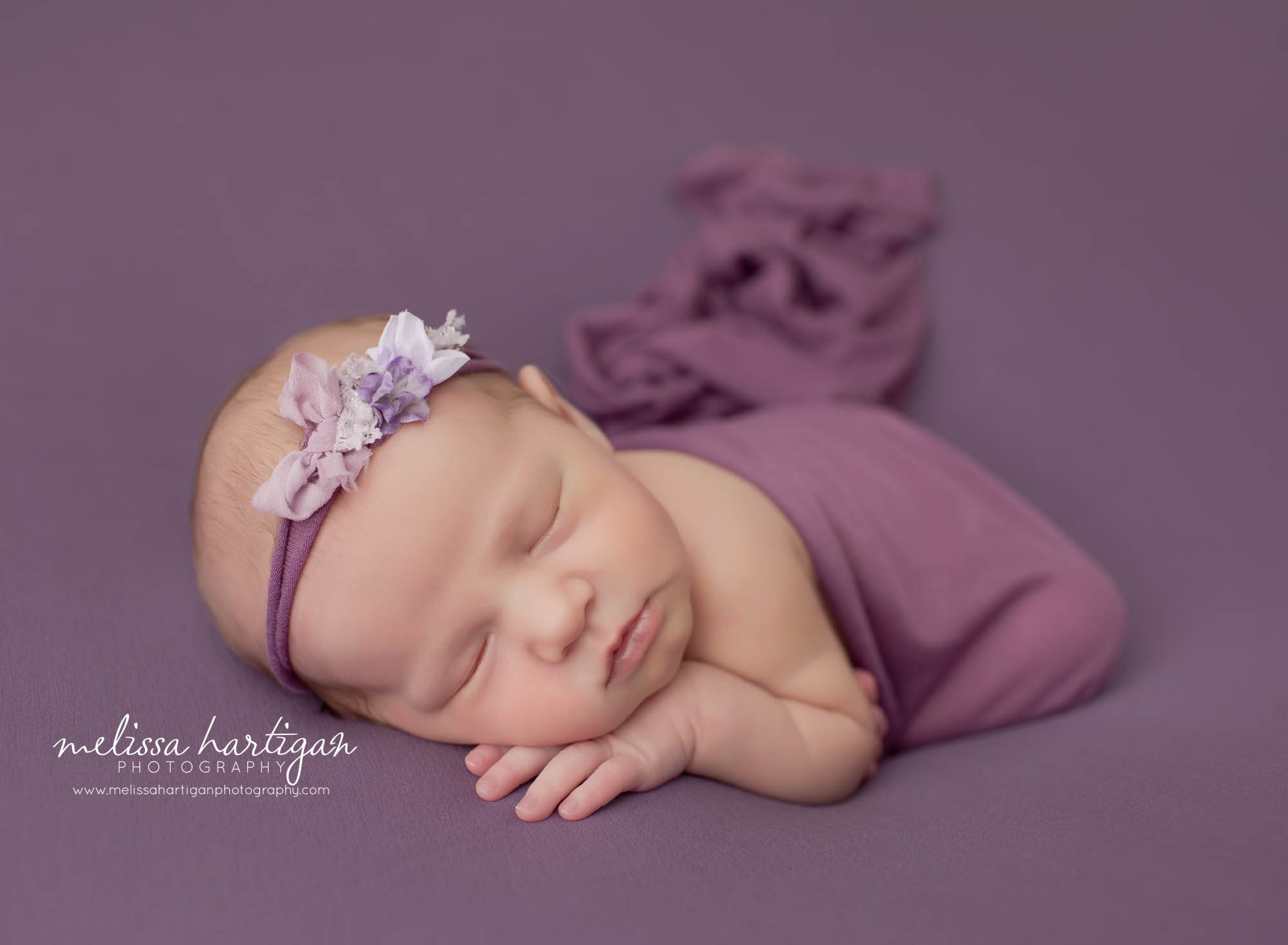 newborn baby girl posed on purple backdrop with flower headband Connecticut newborn photography