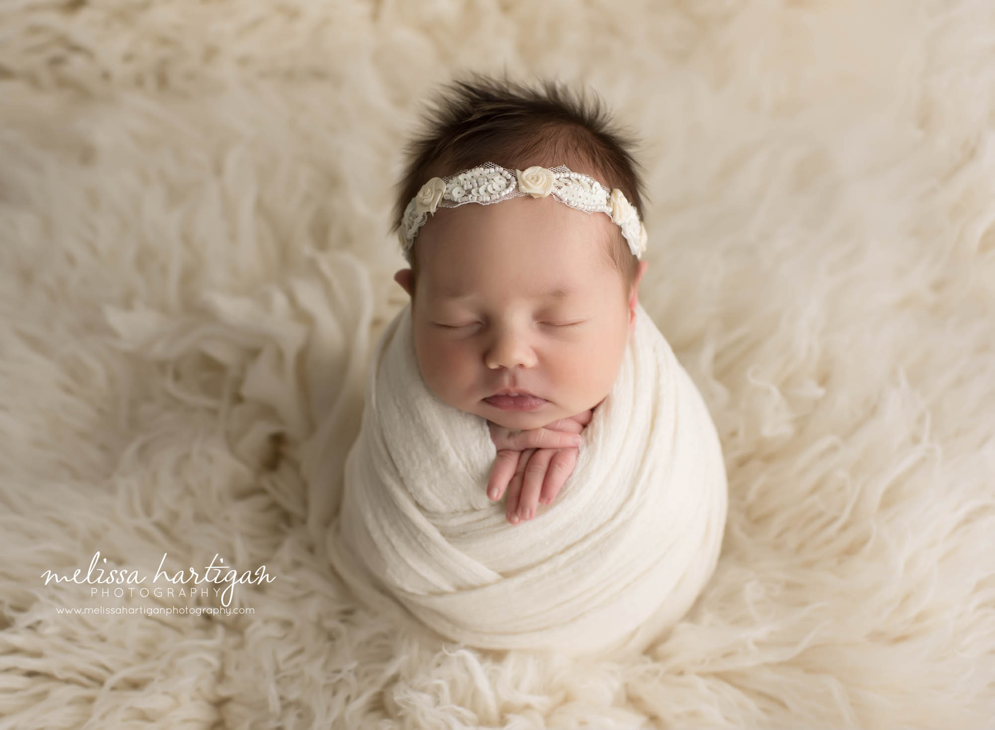 newborn baby girl wrapped in cream wrap with cream headband