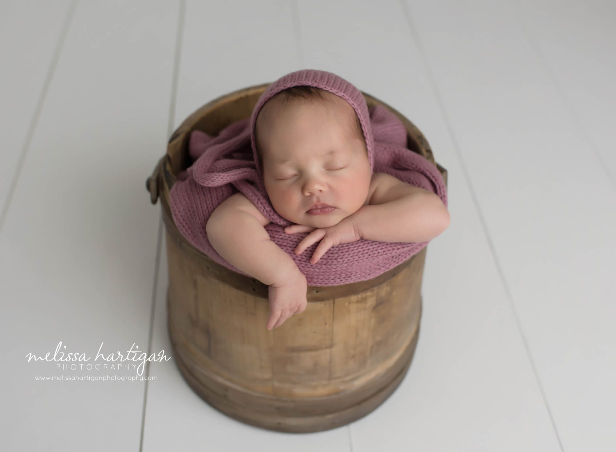 newborn baby girl posed in wooden bucket with pink bonnet and wrap