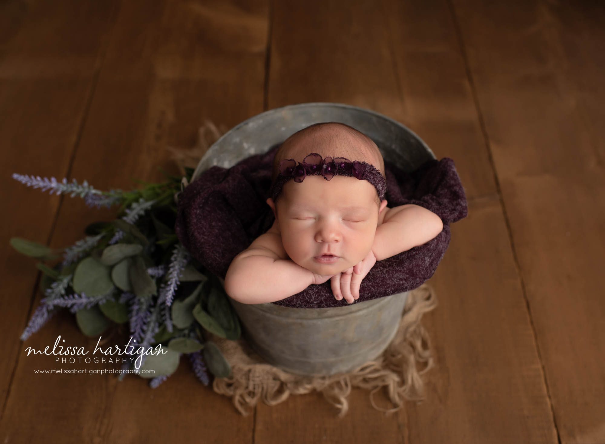newborn baby girl posed in bucket with greenery and floral elements