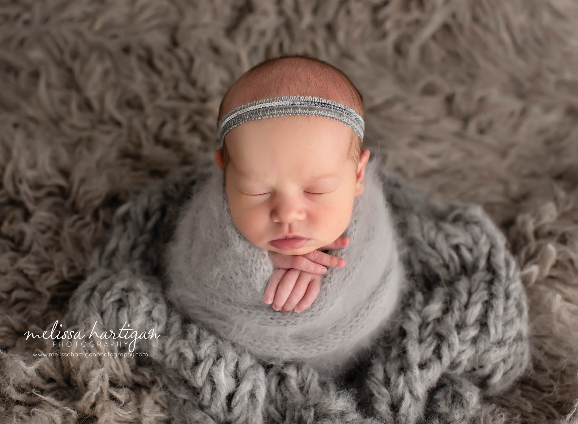newborn baby girl wrapped in knitted gray wrap with headband