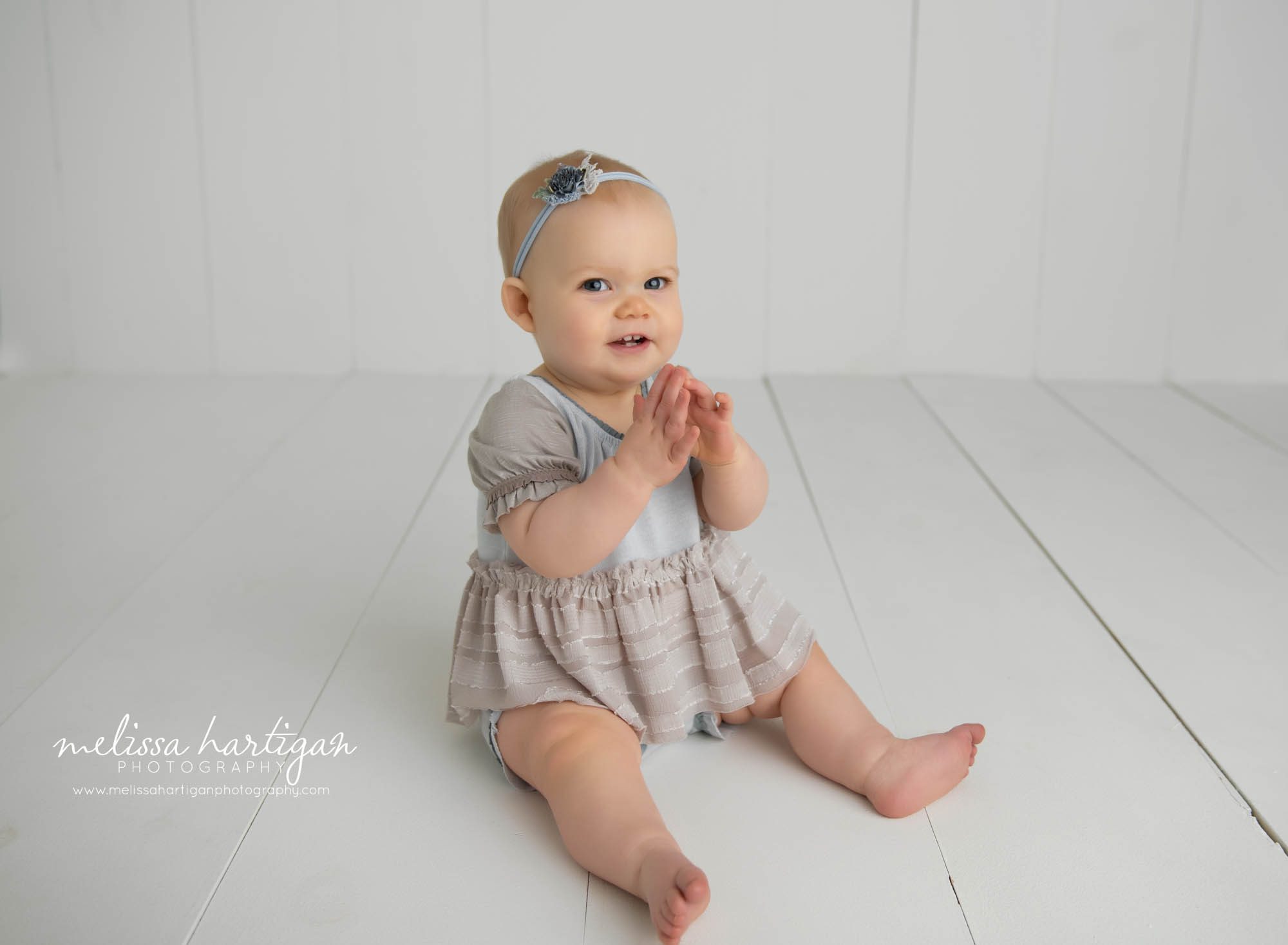 baby girl sitting up on wooden boards wearing blue and tan outfit with headband Amston Baby photographer