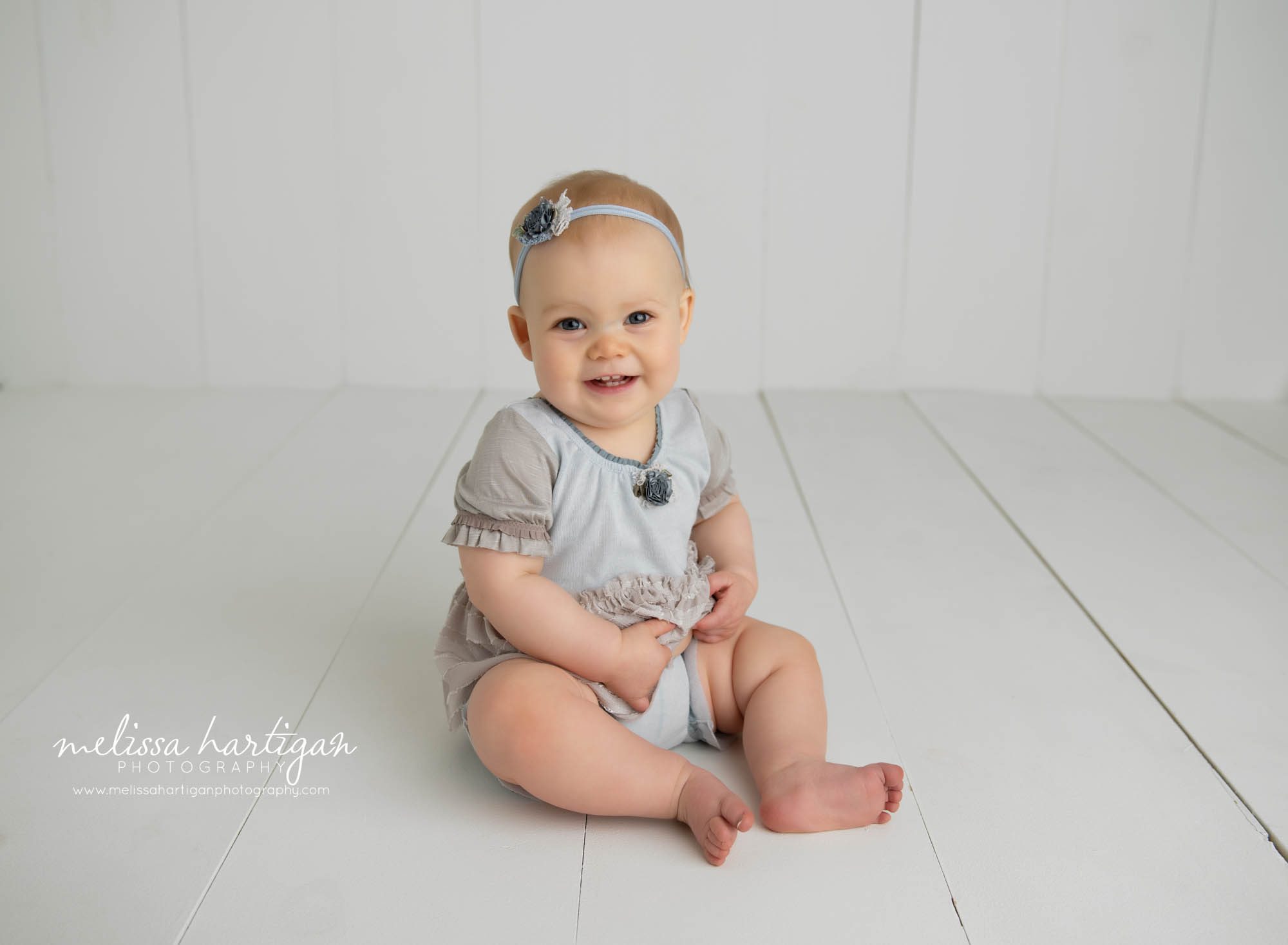 baby girl sitting up on wooden boards wearing blue and tan outfit with headband Amston CT Baby photography