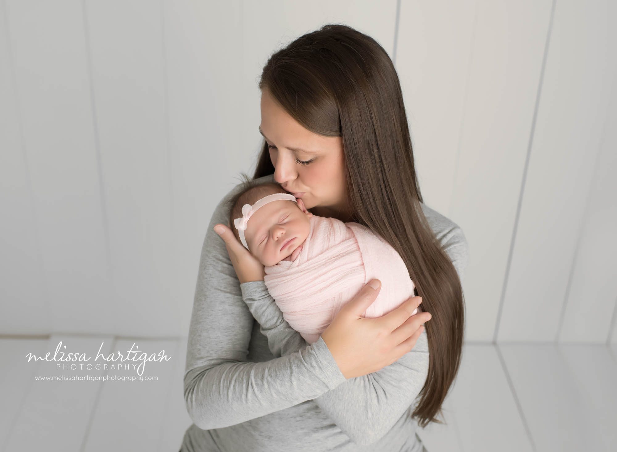 mom holding baby girl kissing newborn daughter on head