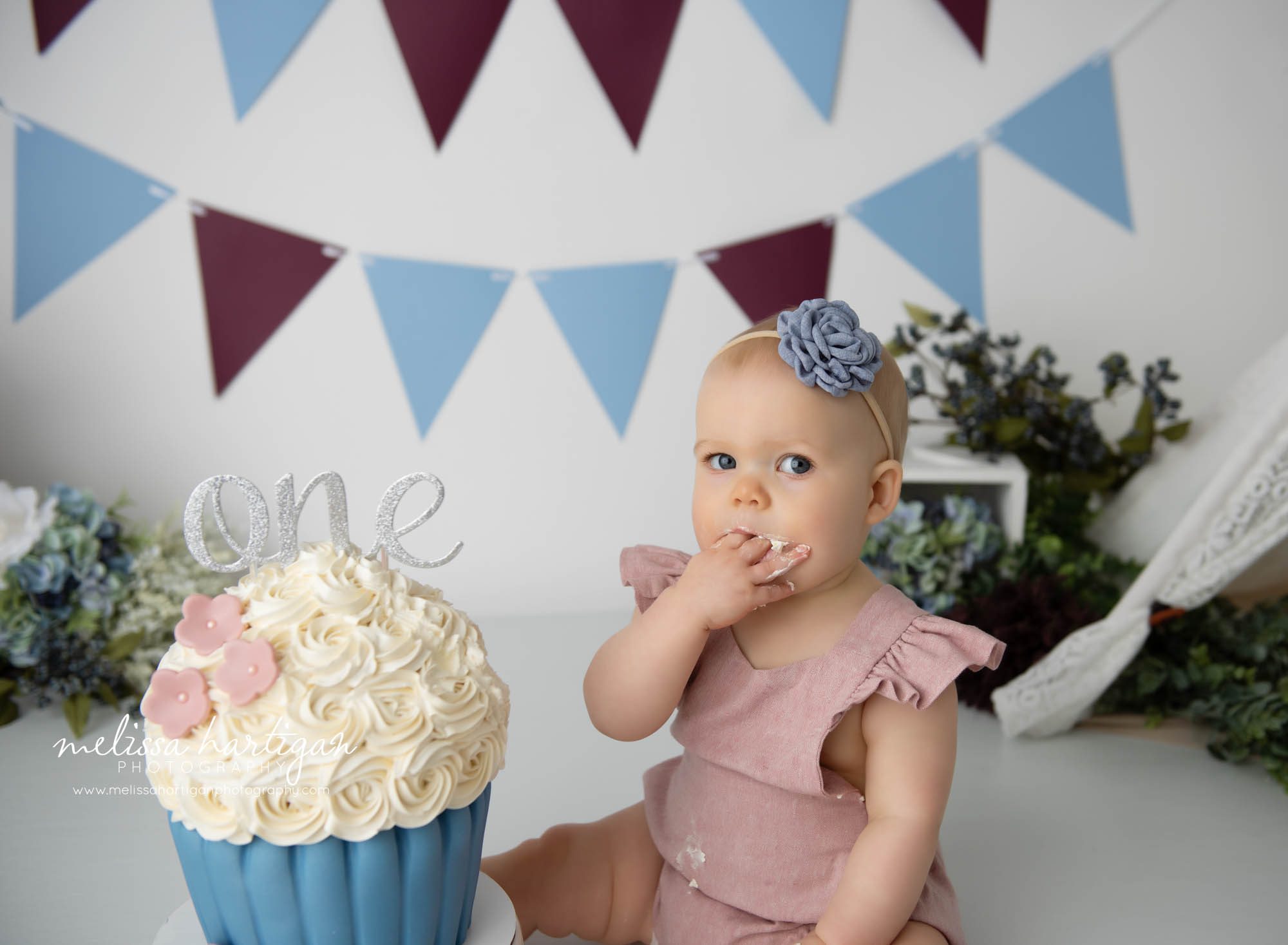 baby girl sitting with fingers in her mouth after tasting cake smash cake