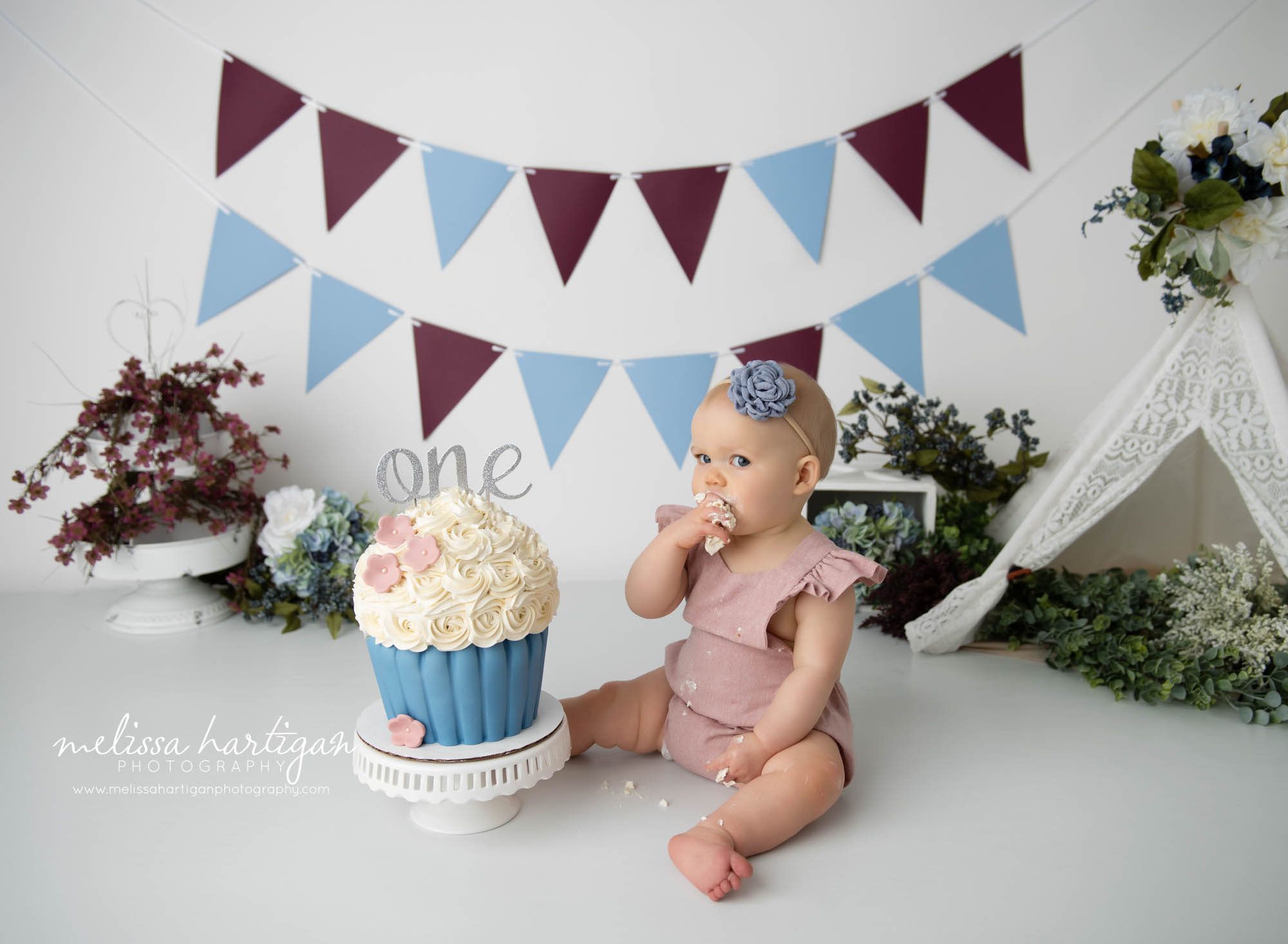 baby girl sitting on floor digging into cake smash cake blue and pink and maroon colors