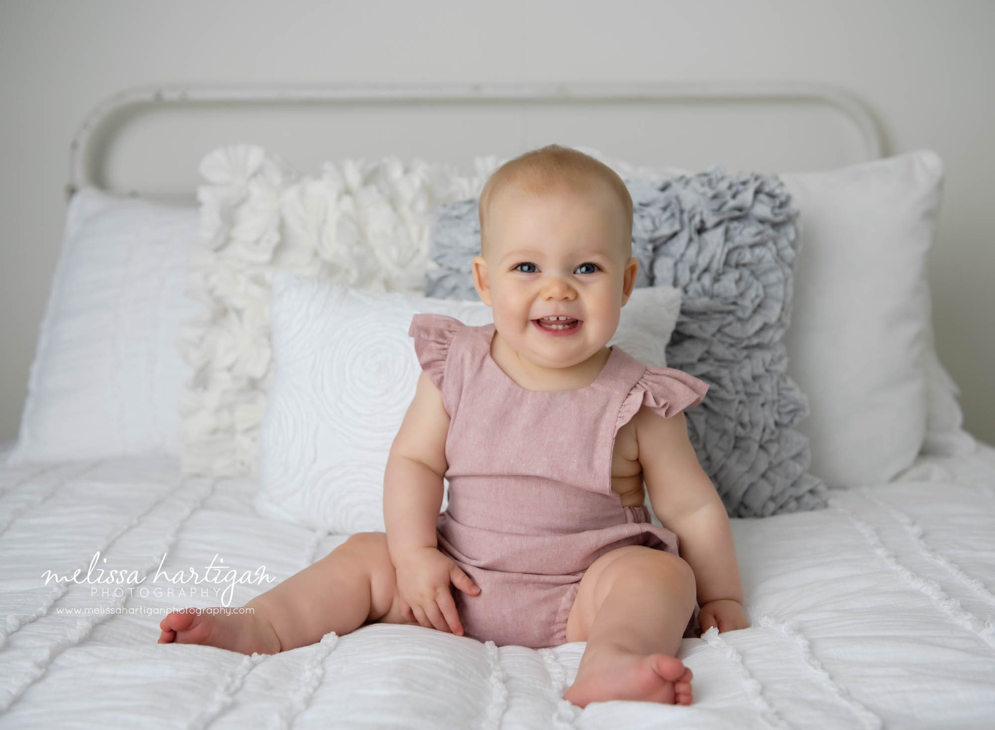 baby girl sitting on bed wearing light pink baby outfit Connecticut baby milestone photographers