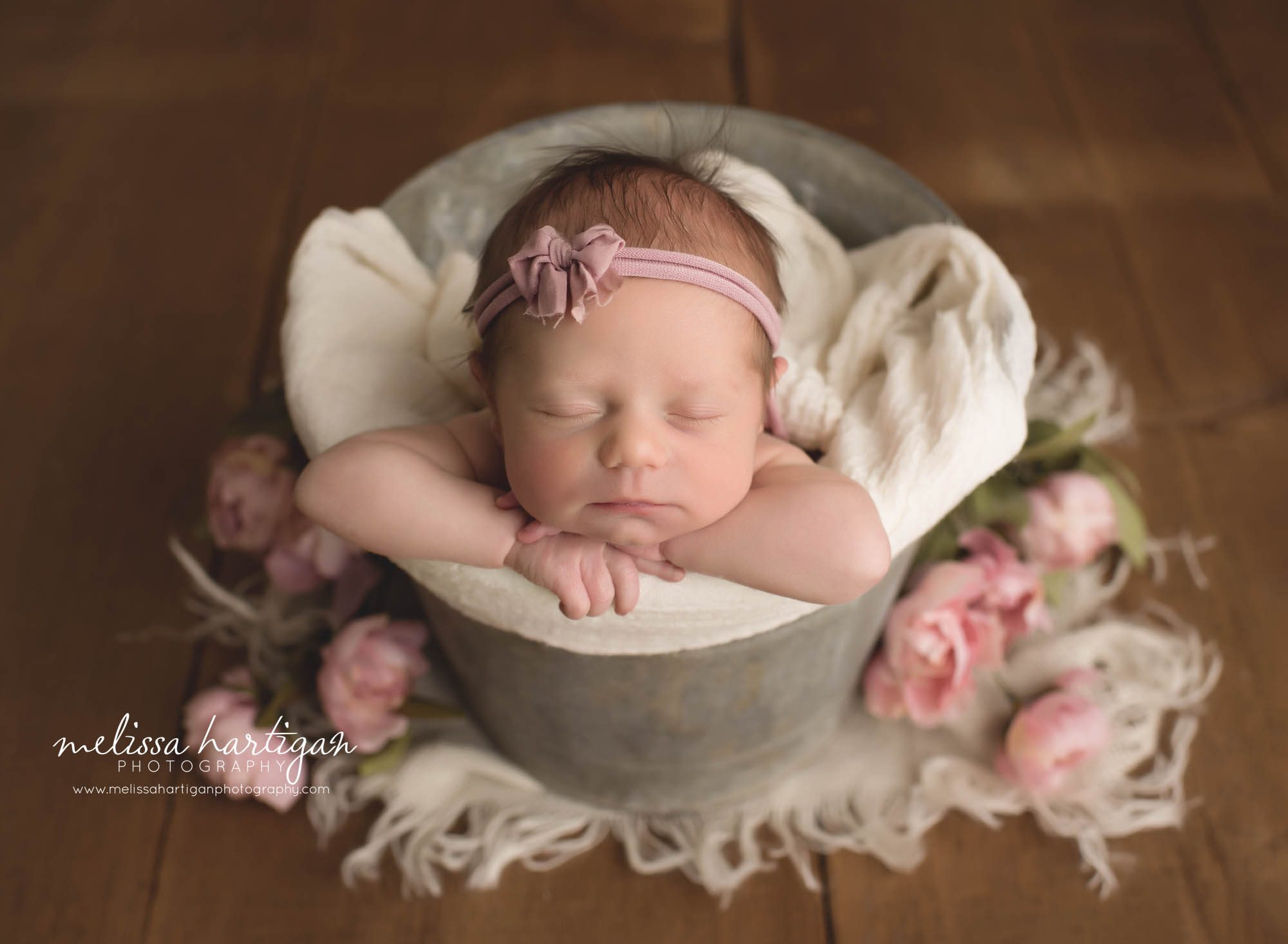 newborn baby girl posed in bucet with floral elements beside bucket